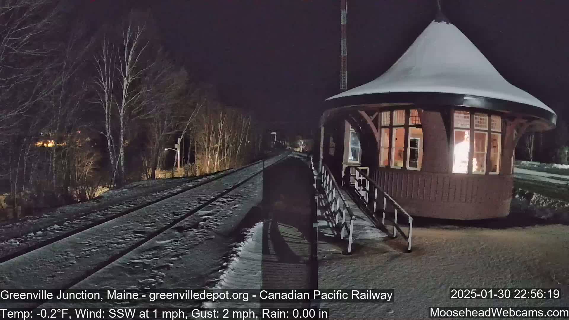 A snow-covered train platform with a lighted building stands next to a set of train tracks at night.