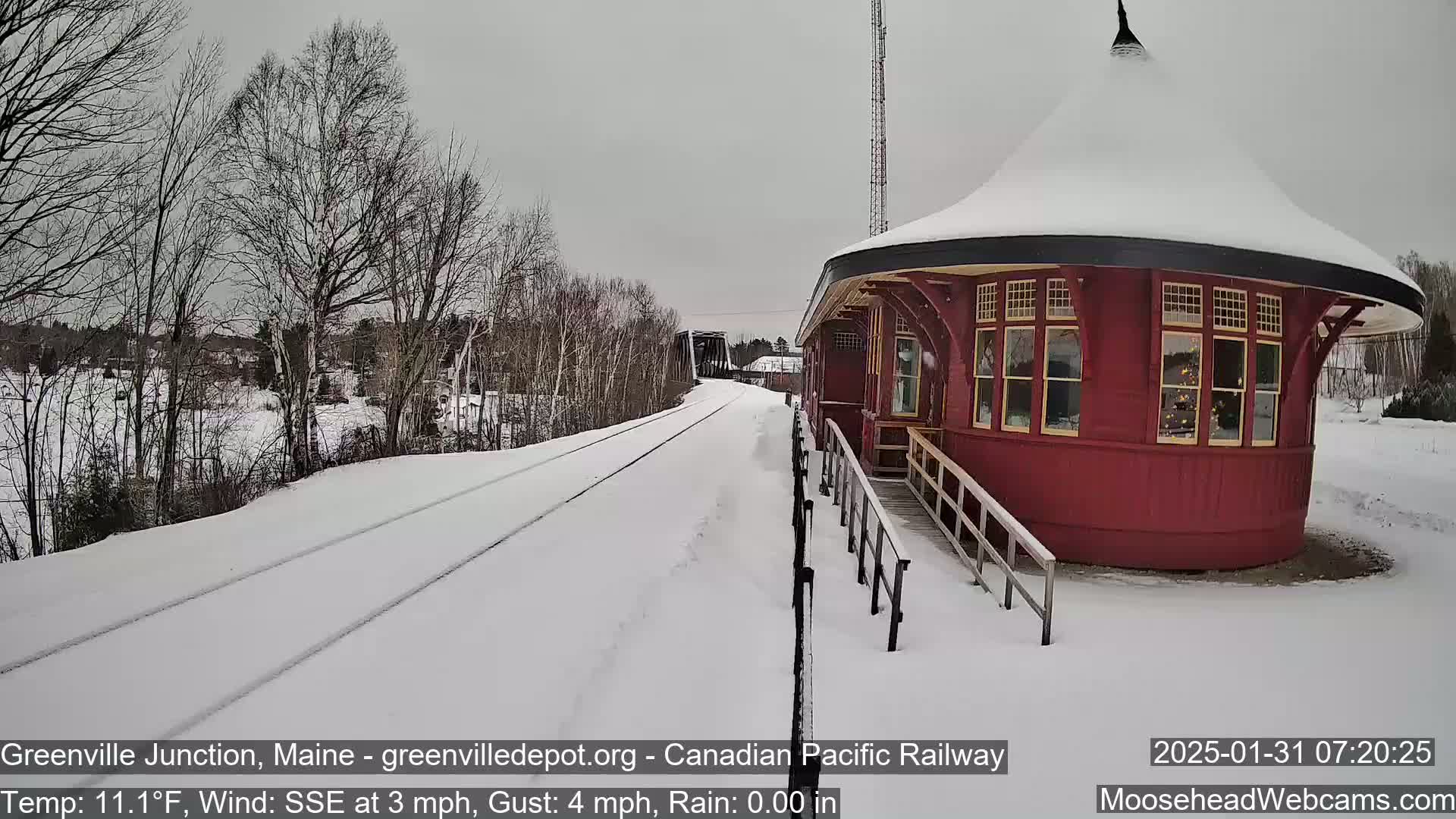 A snow-covered train station with a circular design sits next to a snow-covered railway track on an overcast day.