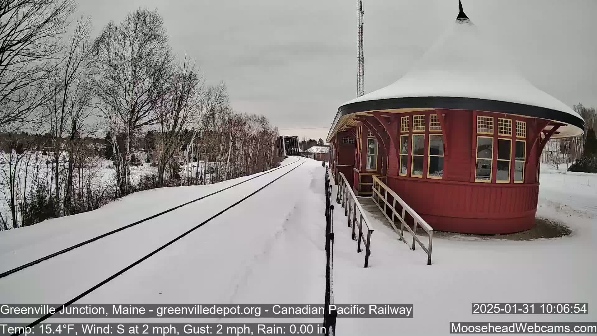 A snow-covered railway track leads to a round, red train depot under a gray sky.