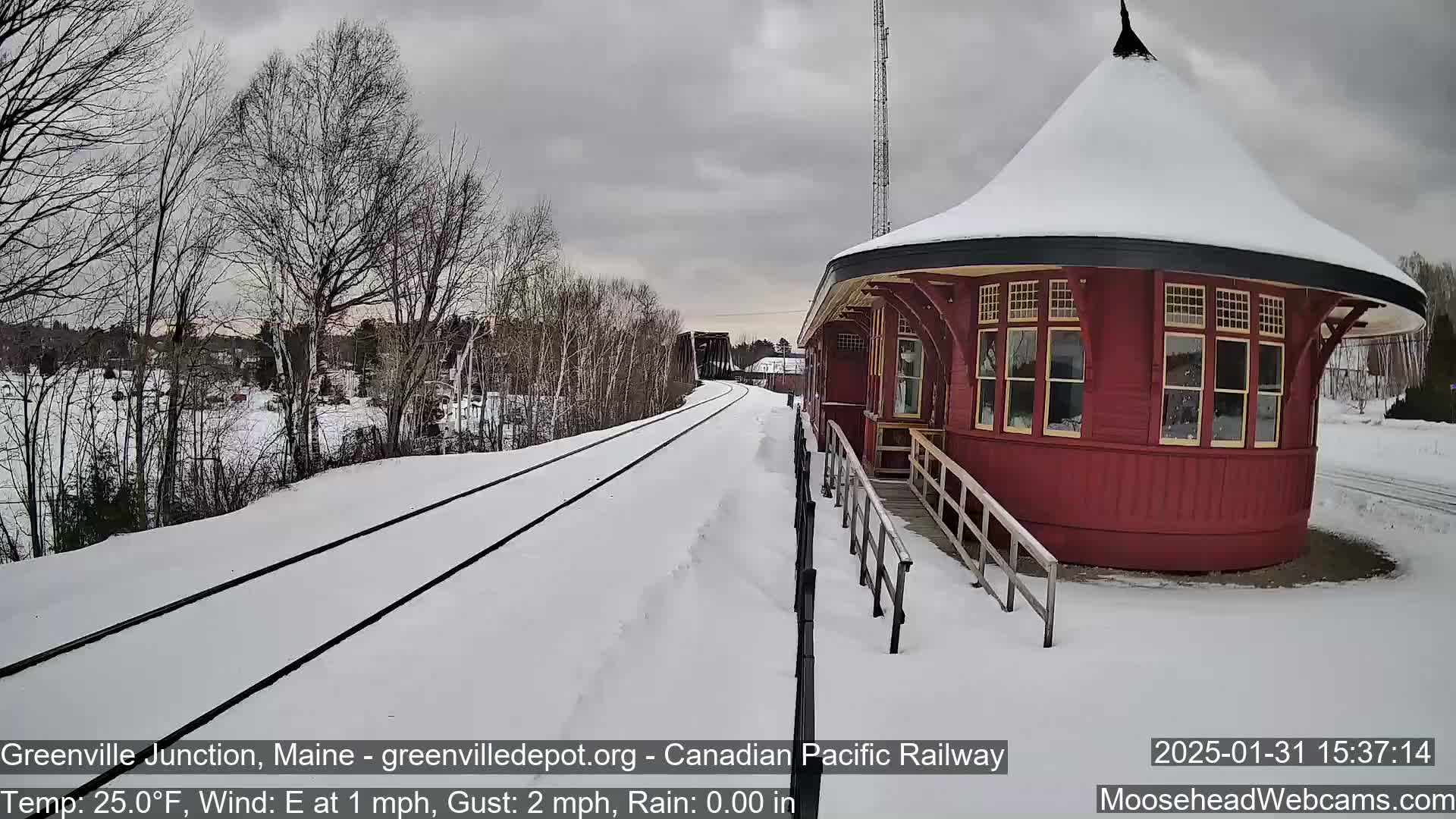 A red, round train depot sits beside snow-covered train tracks on a cloudy day.
