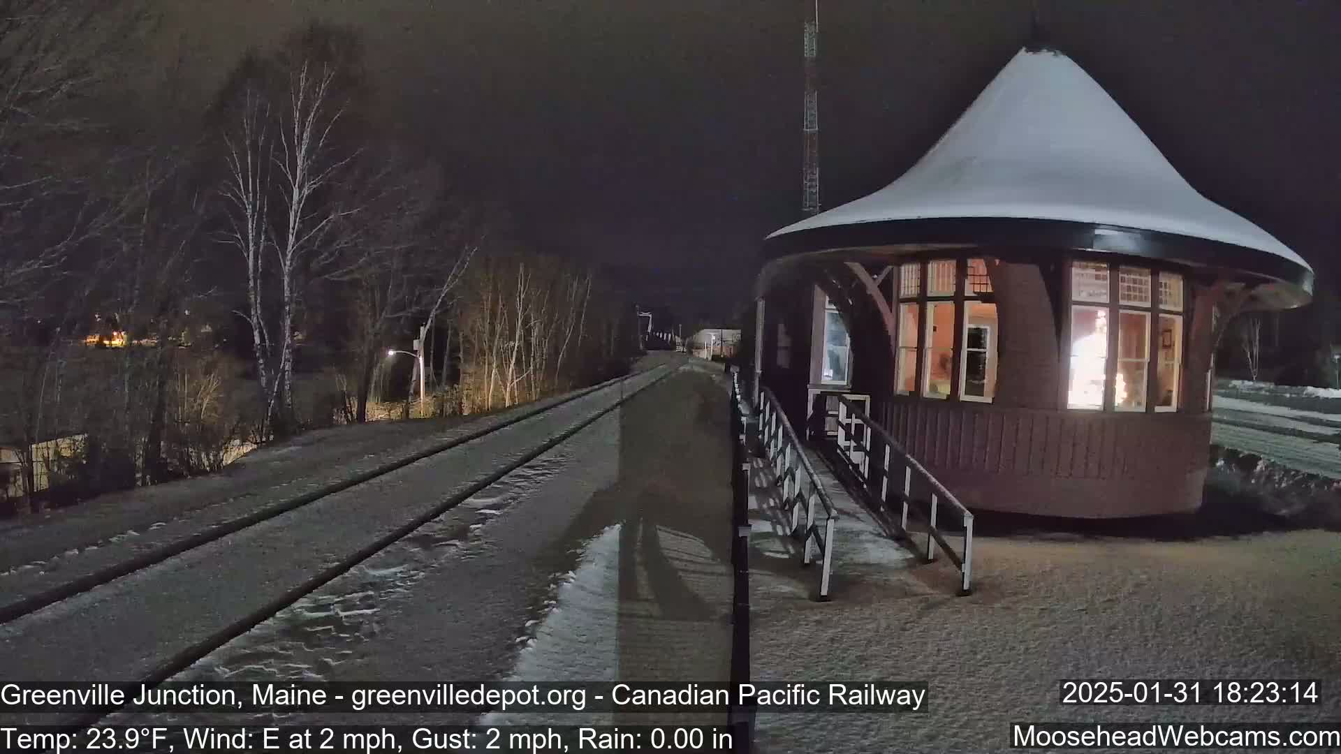 A snow-covered, illuminated train depot sits beside a snow-dusted railway track at night.
