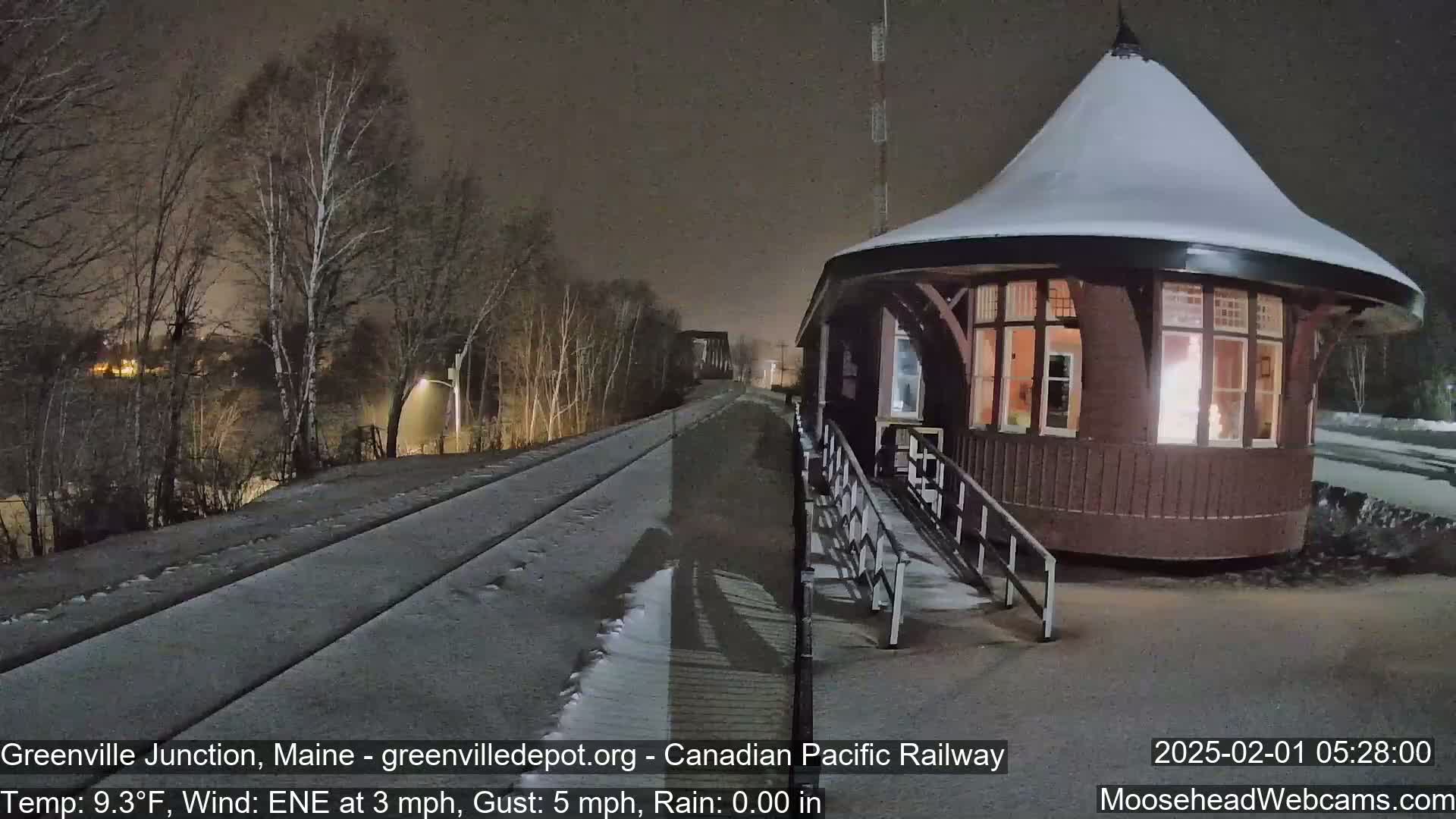 A snow-covered train platform with a round, illuminated building next to a set of train tracks at night.