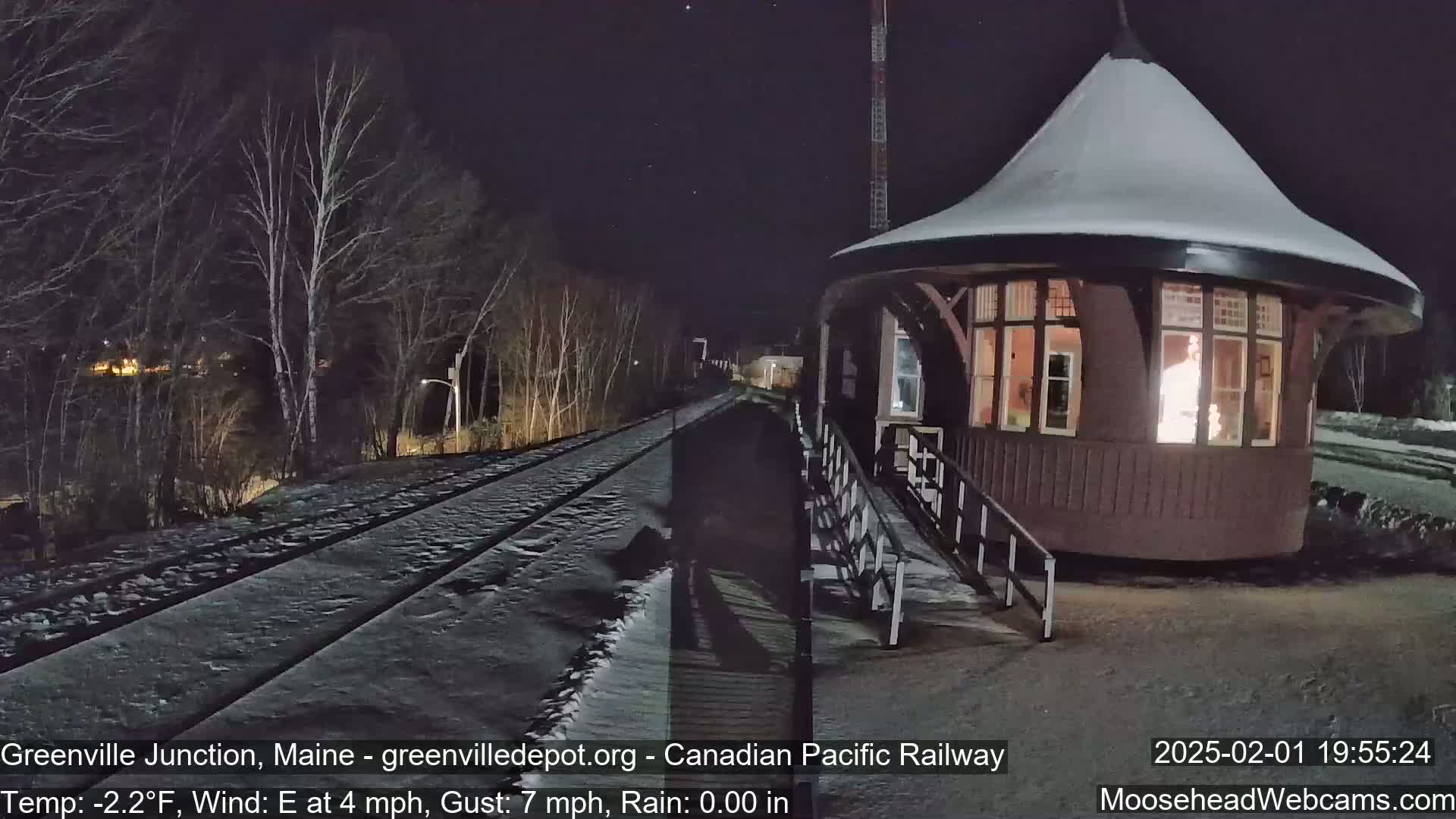 A snow-covered train platform with a lit-up waiting room is visible under a dark, starry night sky.
