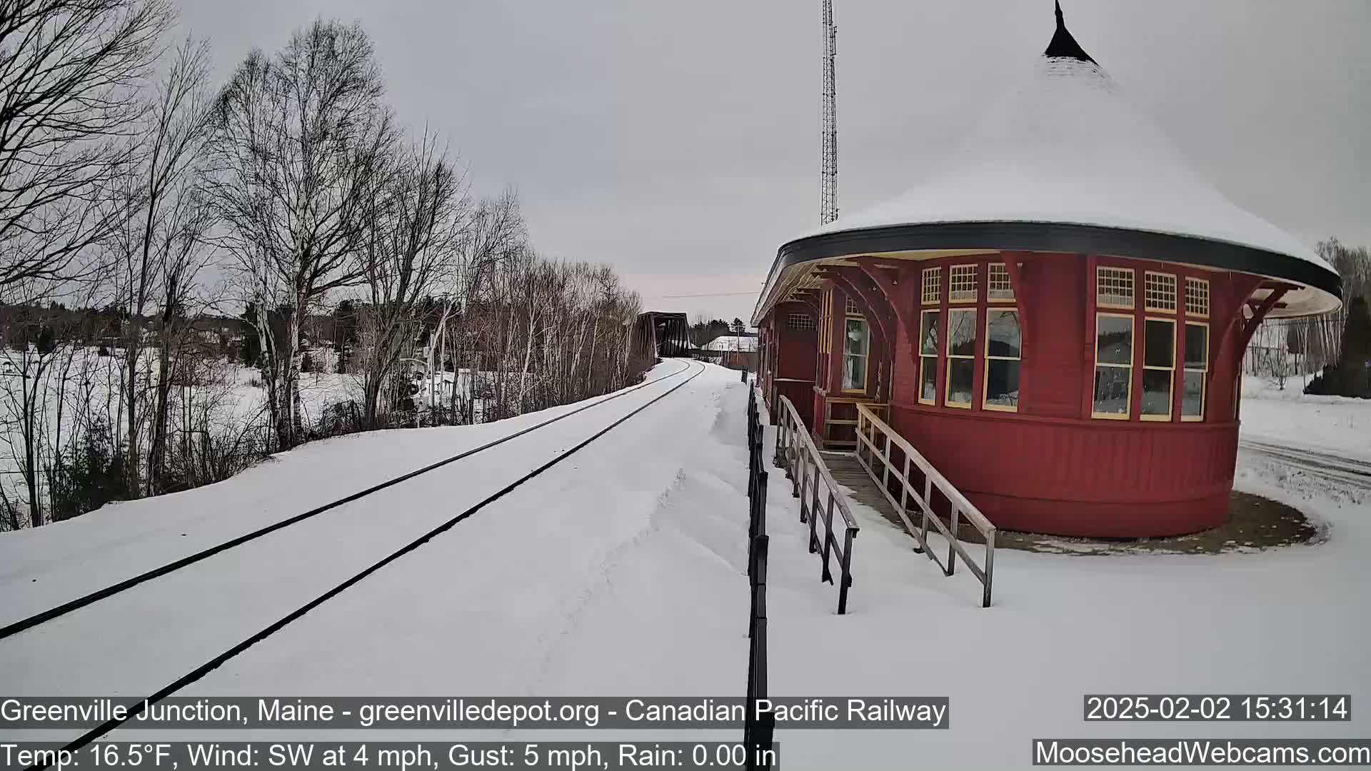 A snow-covered train track leads to a round, red train depot under a gray sky.