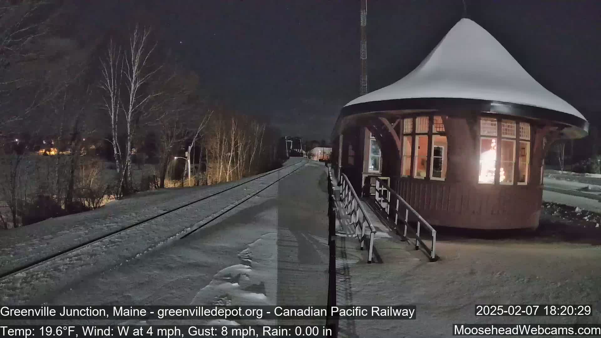 A snow-covered train platform with a small, illuminated building at night, under a clear sky.