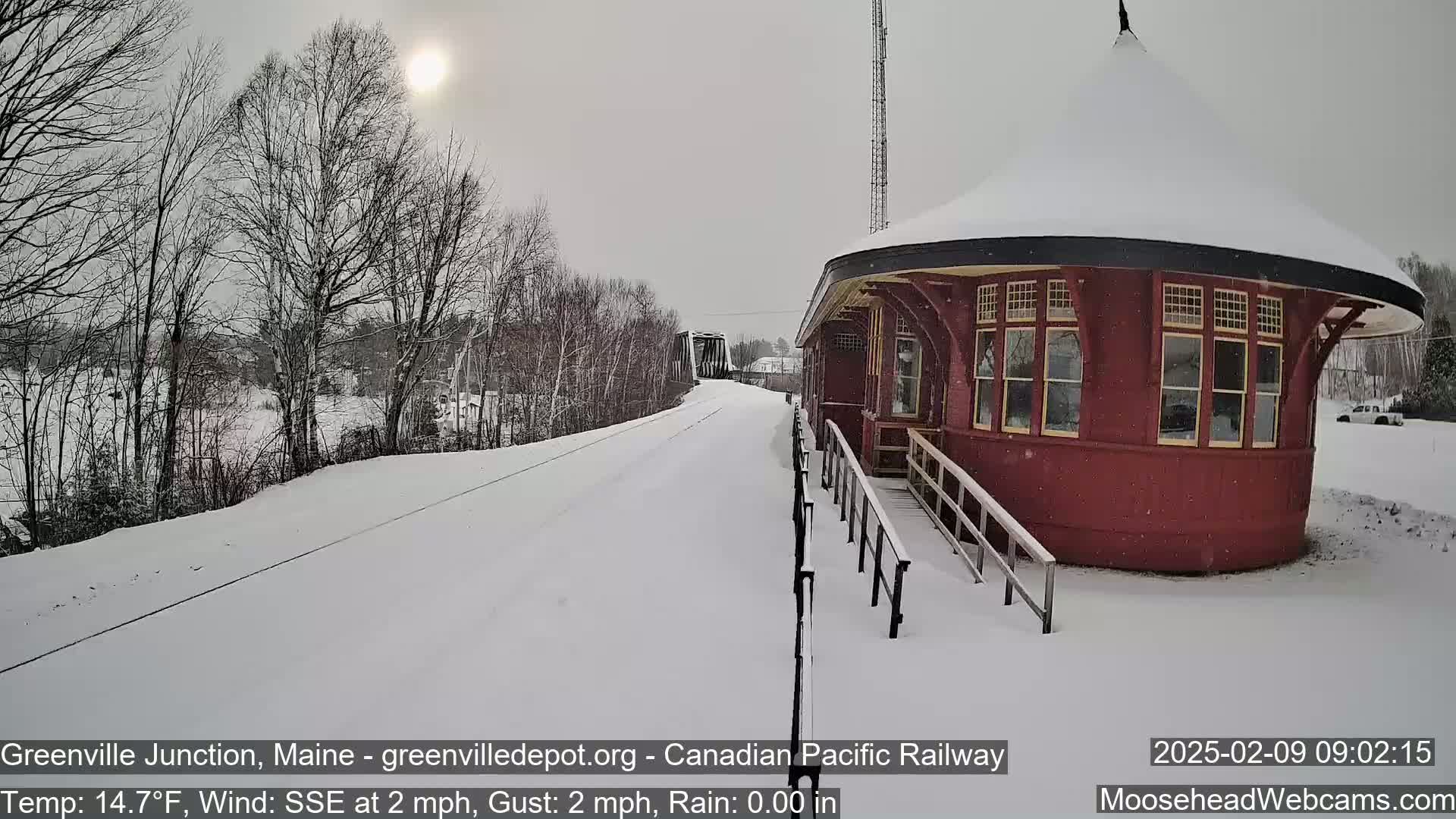 A snow-covered train depot with a circular design sits beside a snow-covered railway track under a bright, sunny sky.