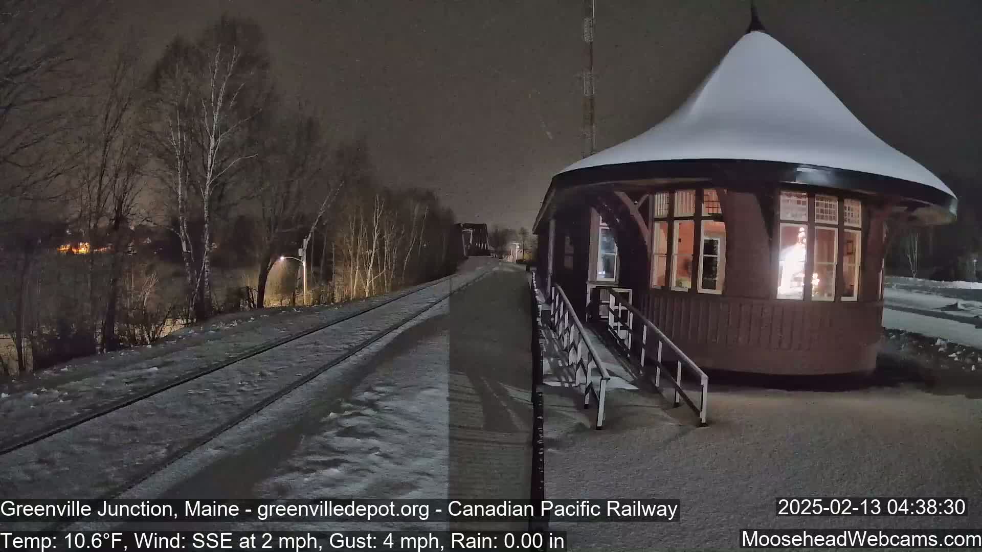 A snow-covered train station platform and tracks are visible at night under a dark sky.