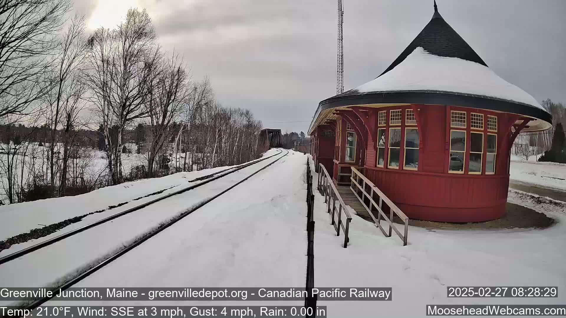 A snow-covered train track leads to a red, round train station under a cloudy sky.