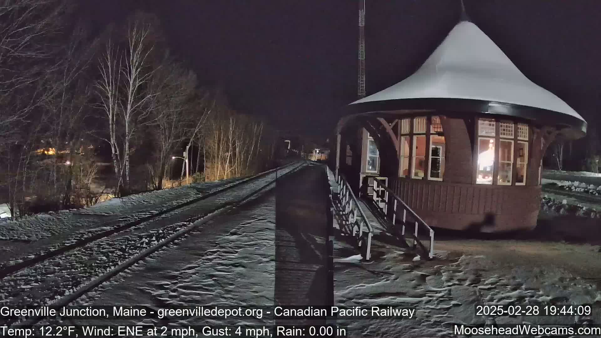 A snow-covered train platform and a round, dark-brown train station are illuminated at night under a clear sky.