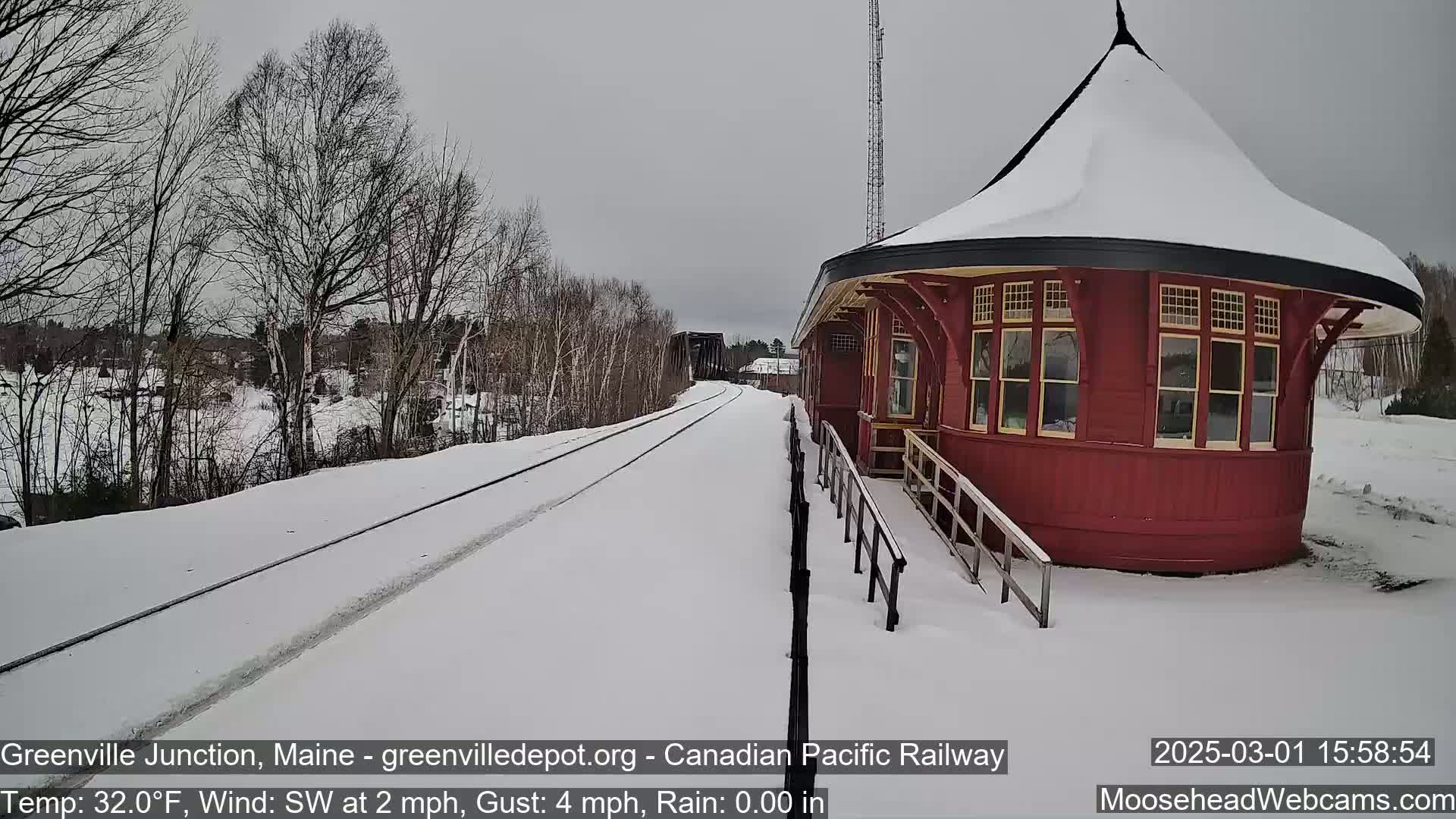 A snow-covered train track leads to a red, round train station under a gray sky.