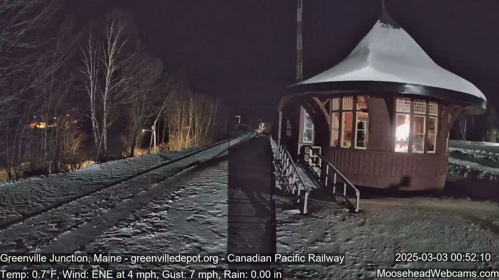 A snow-covered, round train station is illuminated at night, next to a snow-covered railway track under a dark sky.