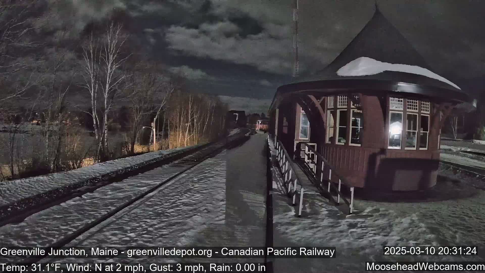 A snow-covered train platform and tracks are visible under a dark, cloudy night sky.