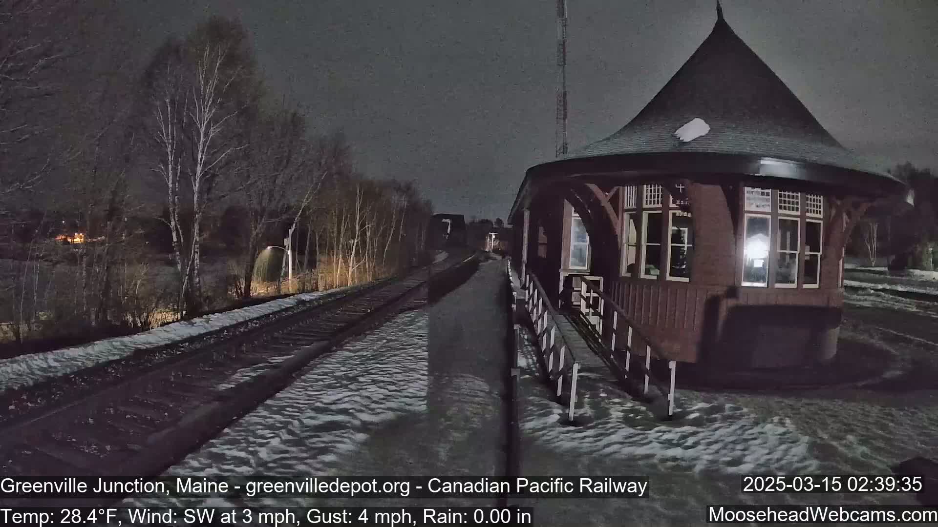 A snow-covered train platform and a dark red octagonal building are visible at night under a dark sky.