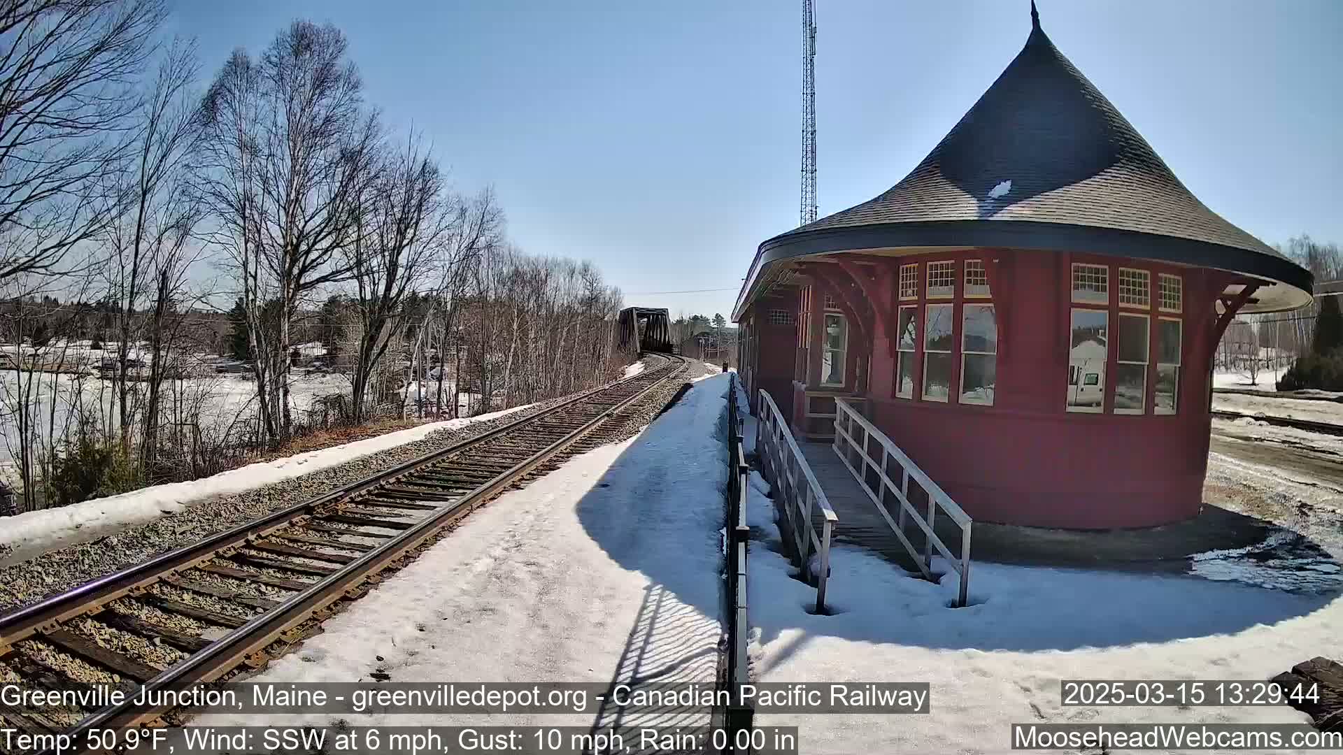A red train depot sits beside snow-covered railroad tracks on a sunny day with a light south-southwesterly wind.