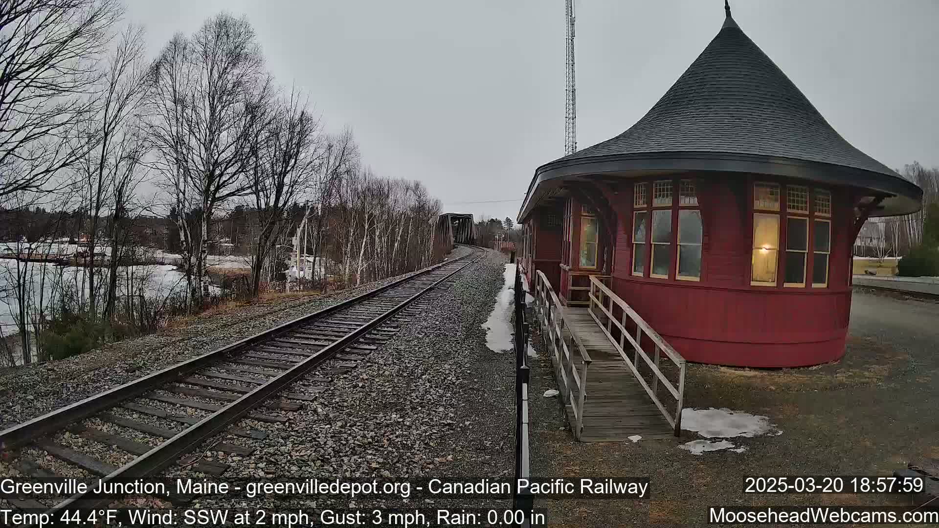 A red, round train depot with a conical roof sits beside railroad tracks on an overcast day.