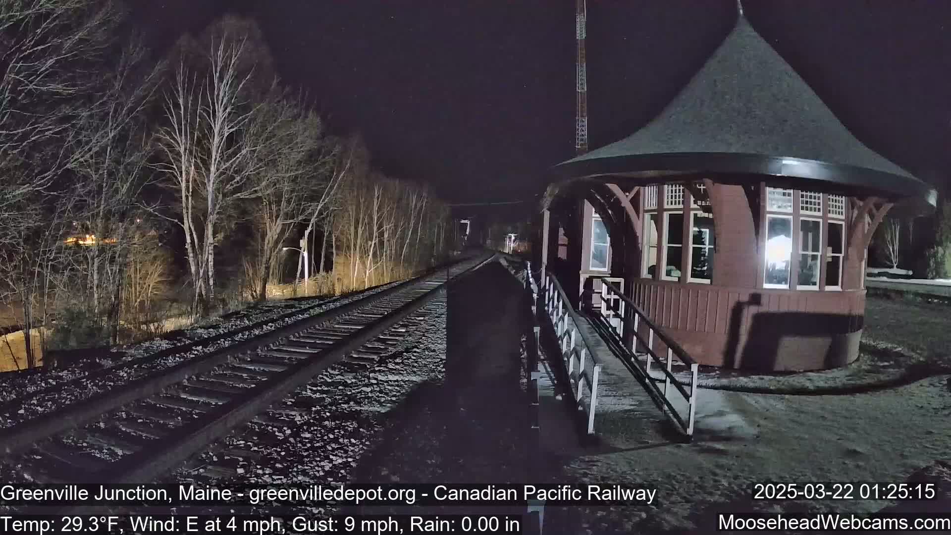 A dark brown, octagonal train depot stands next to a set of train tracks at night under a clear, dark sky.