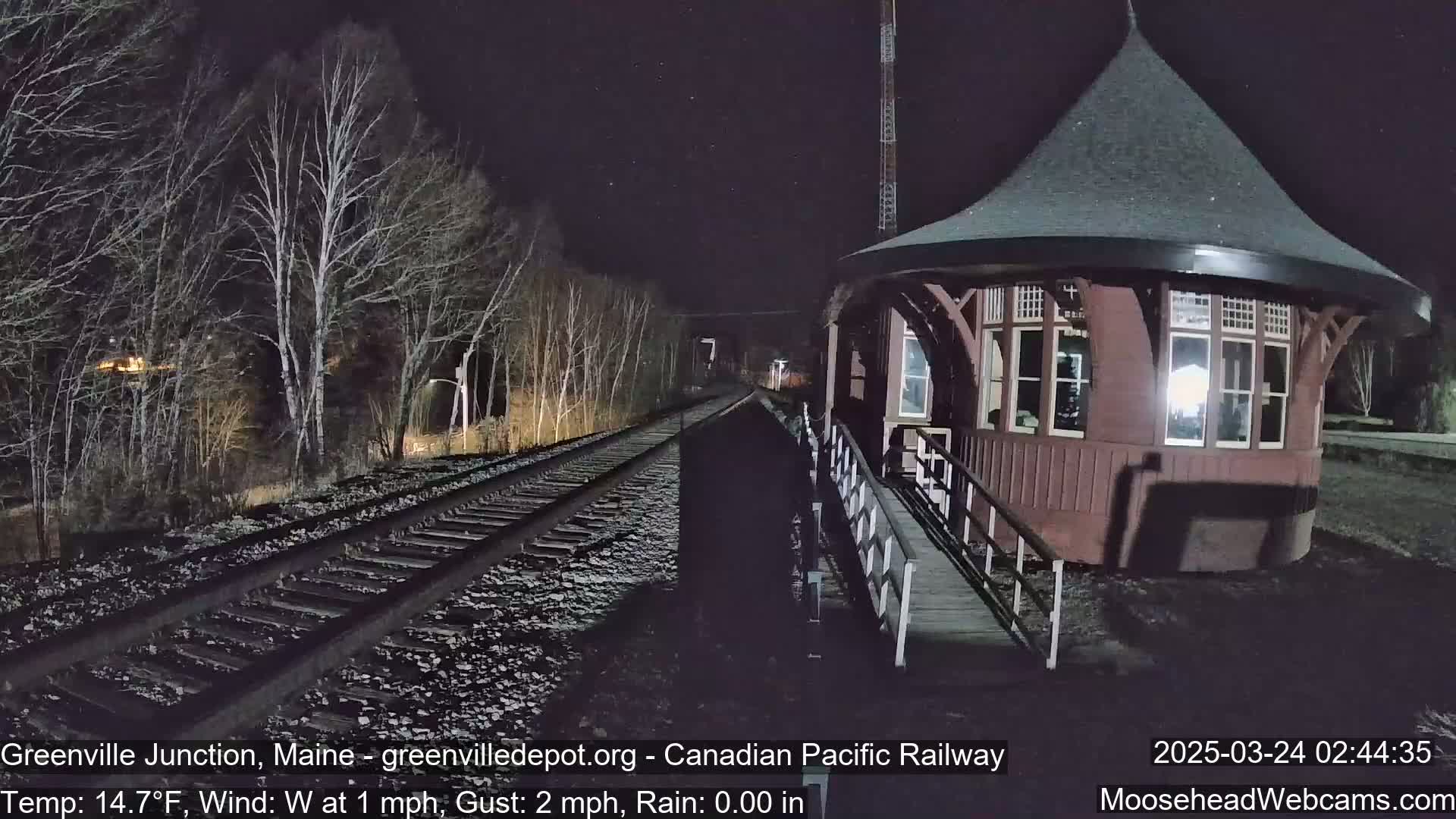 A dark, nighttime scene shows a red octagonal train depot next to train tracks that lead into a forest of bare trees under a lightly starry sky.