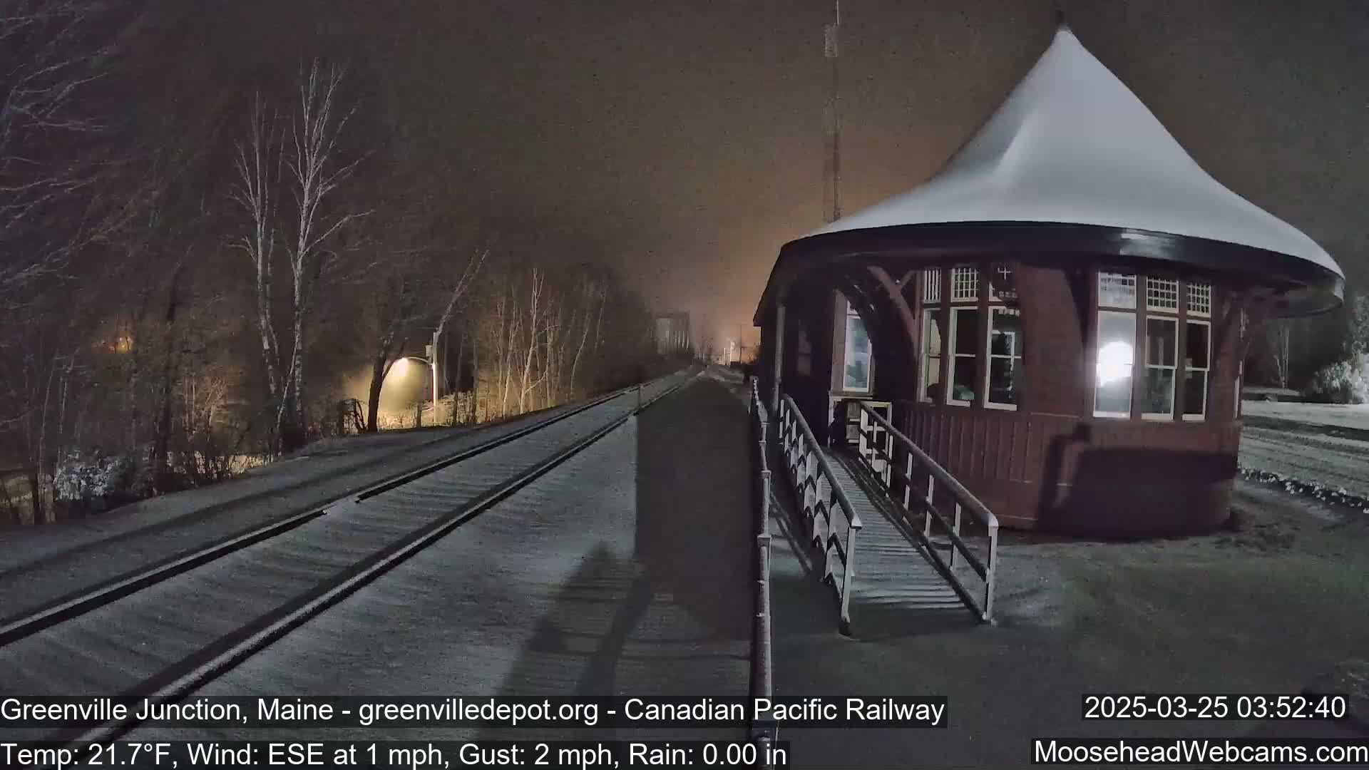 A snow-covered train platform and a small, snow-capped, octagonal building are visible under a dark, snowy night sky.