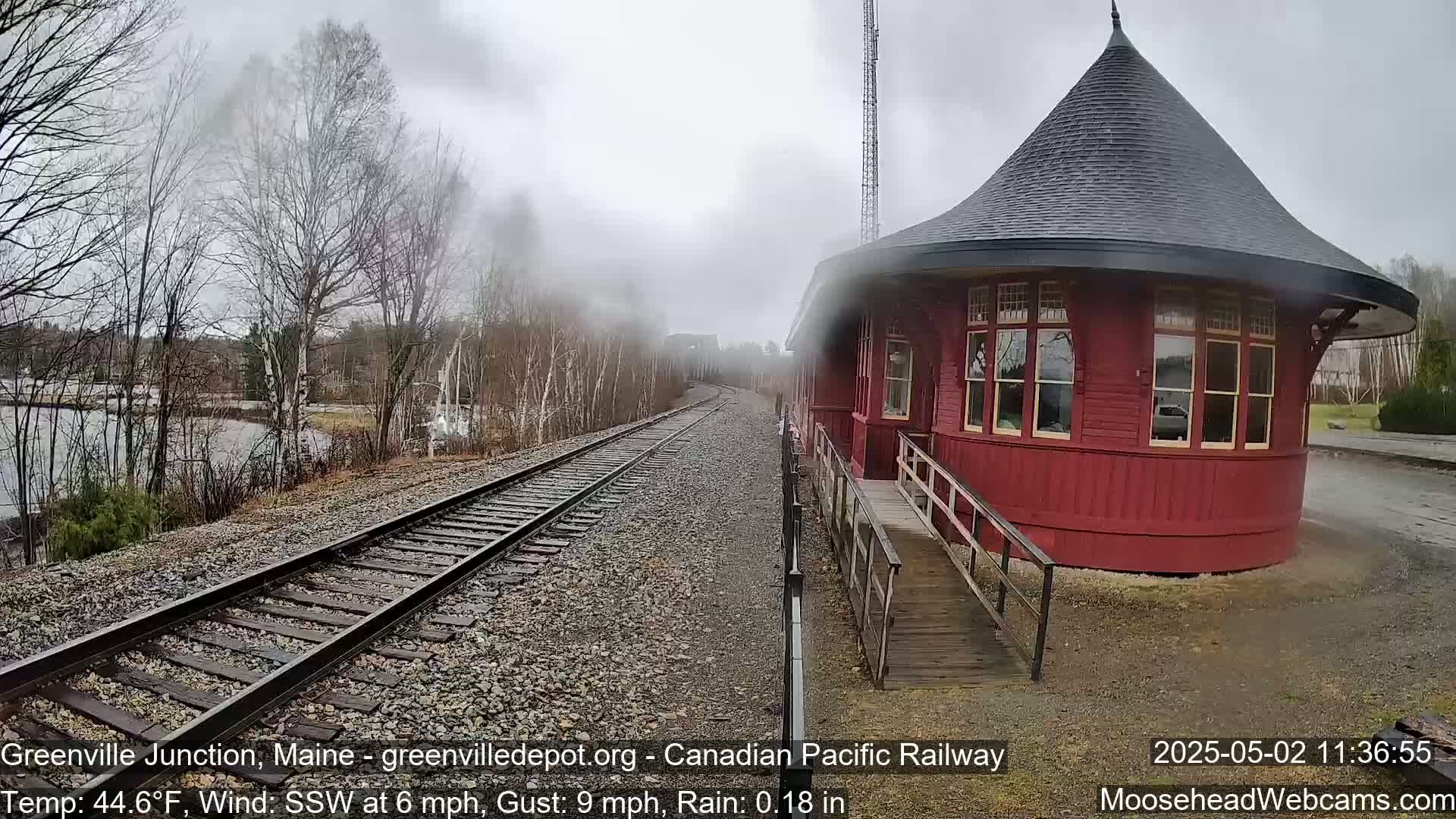 A red, round train station sits beside railroad tracks on a rainy day with a light mist.