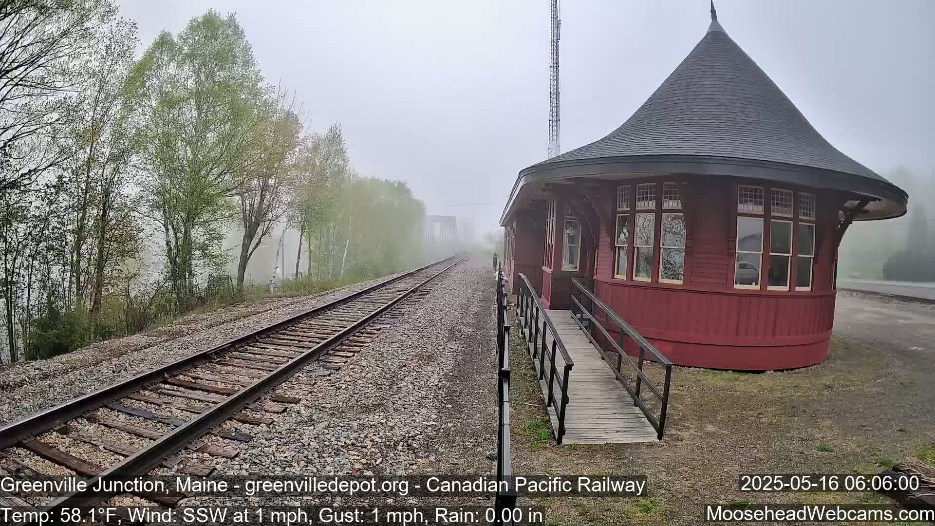 A red, round train depot with a conical roof stands beside railroad tracks on a foggy morning.