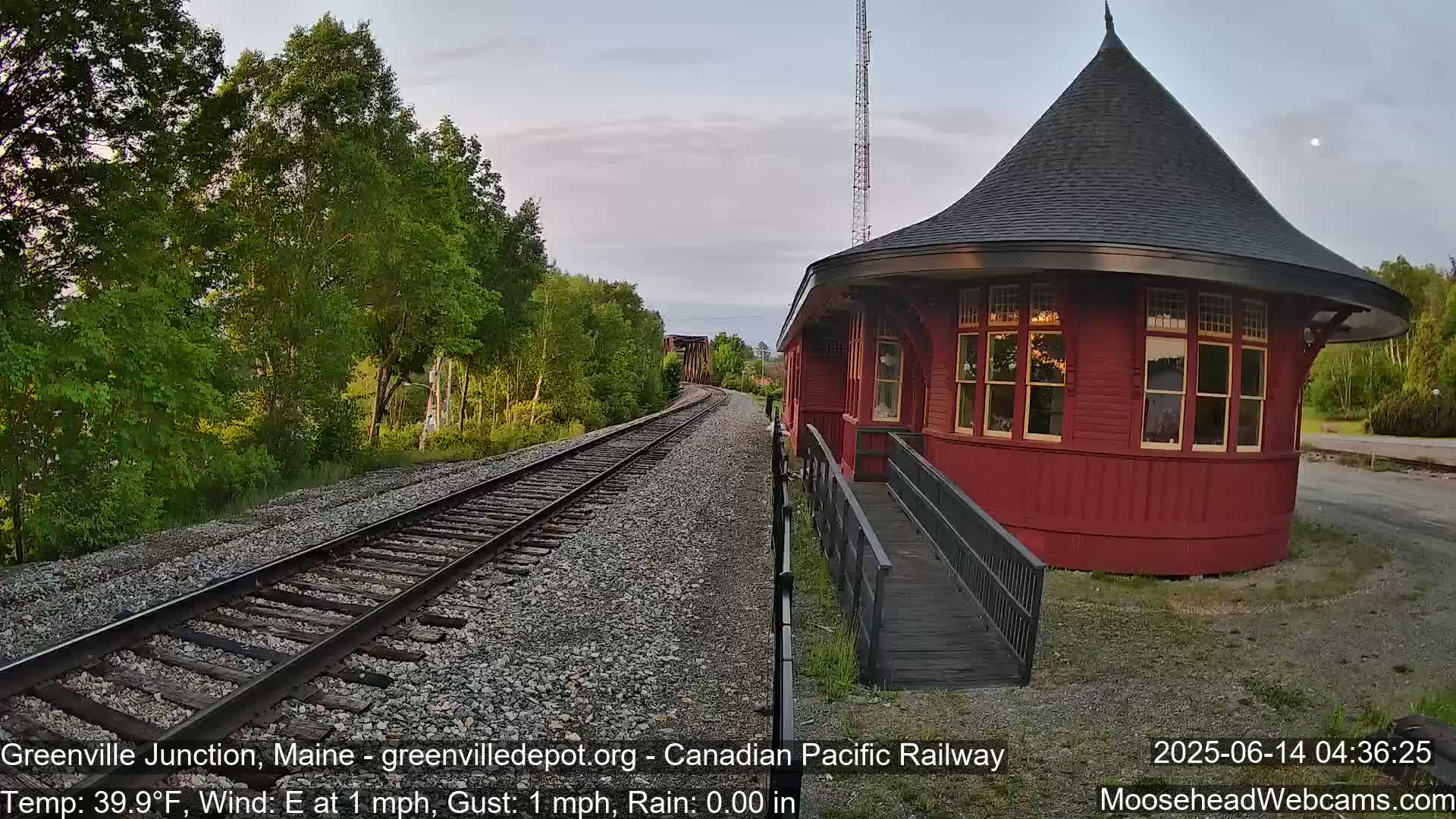 A red, round train depot sits beside railroad tracks curving into the distance under a mostly clear, twilight sky.