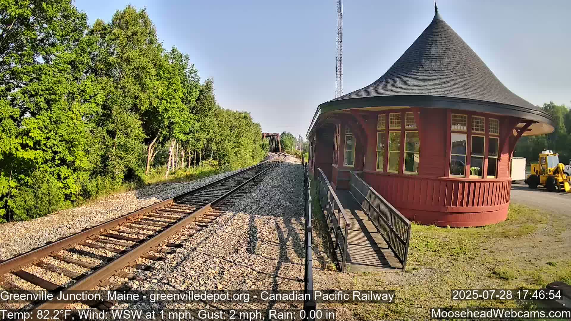 A red octagonal train depot sits beside train tracks on a sunny day with a light wind.