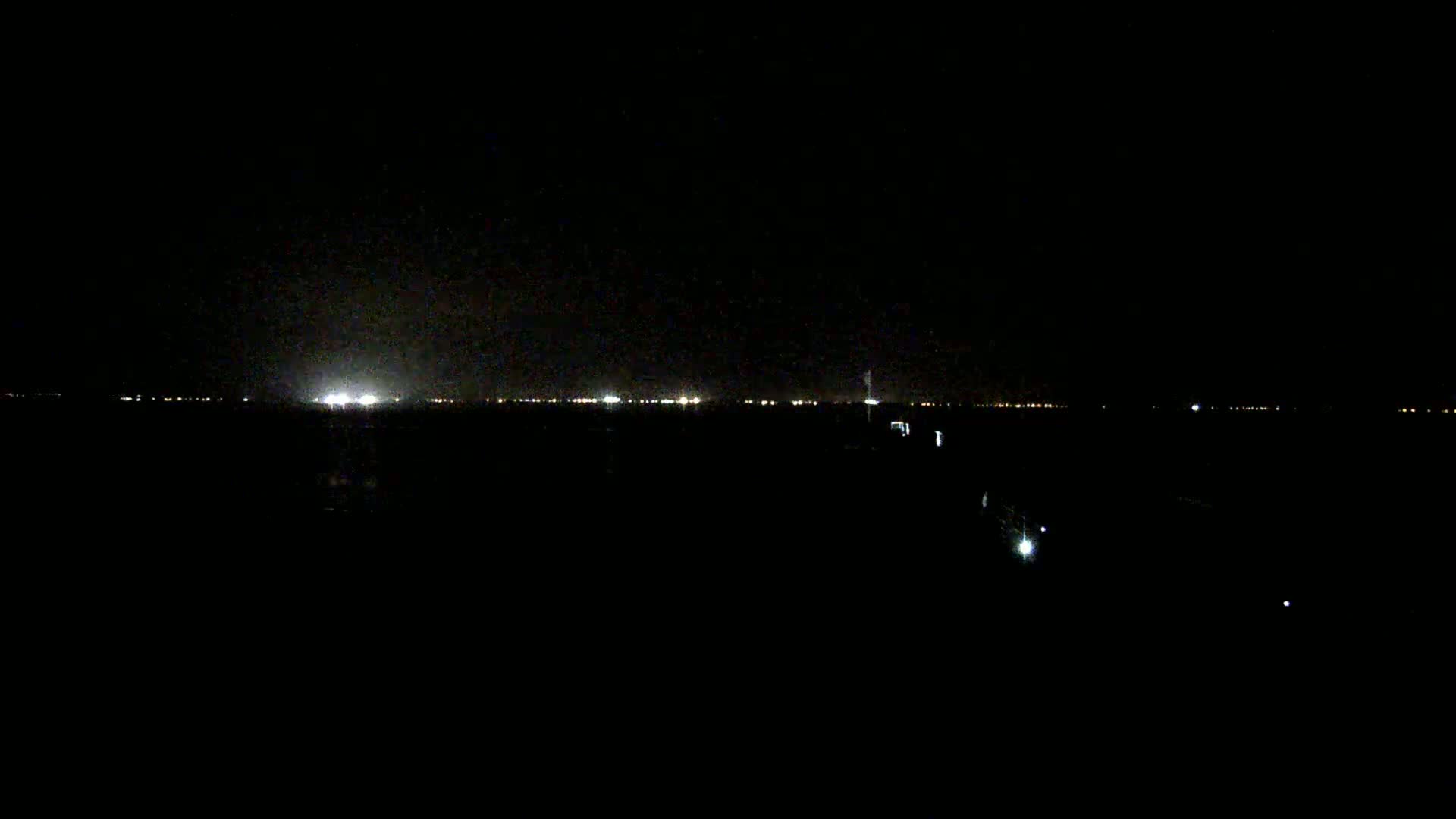 A dark, nighttime scene shows a distant line of lights across a flat landscape under a clear, dark sky.