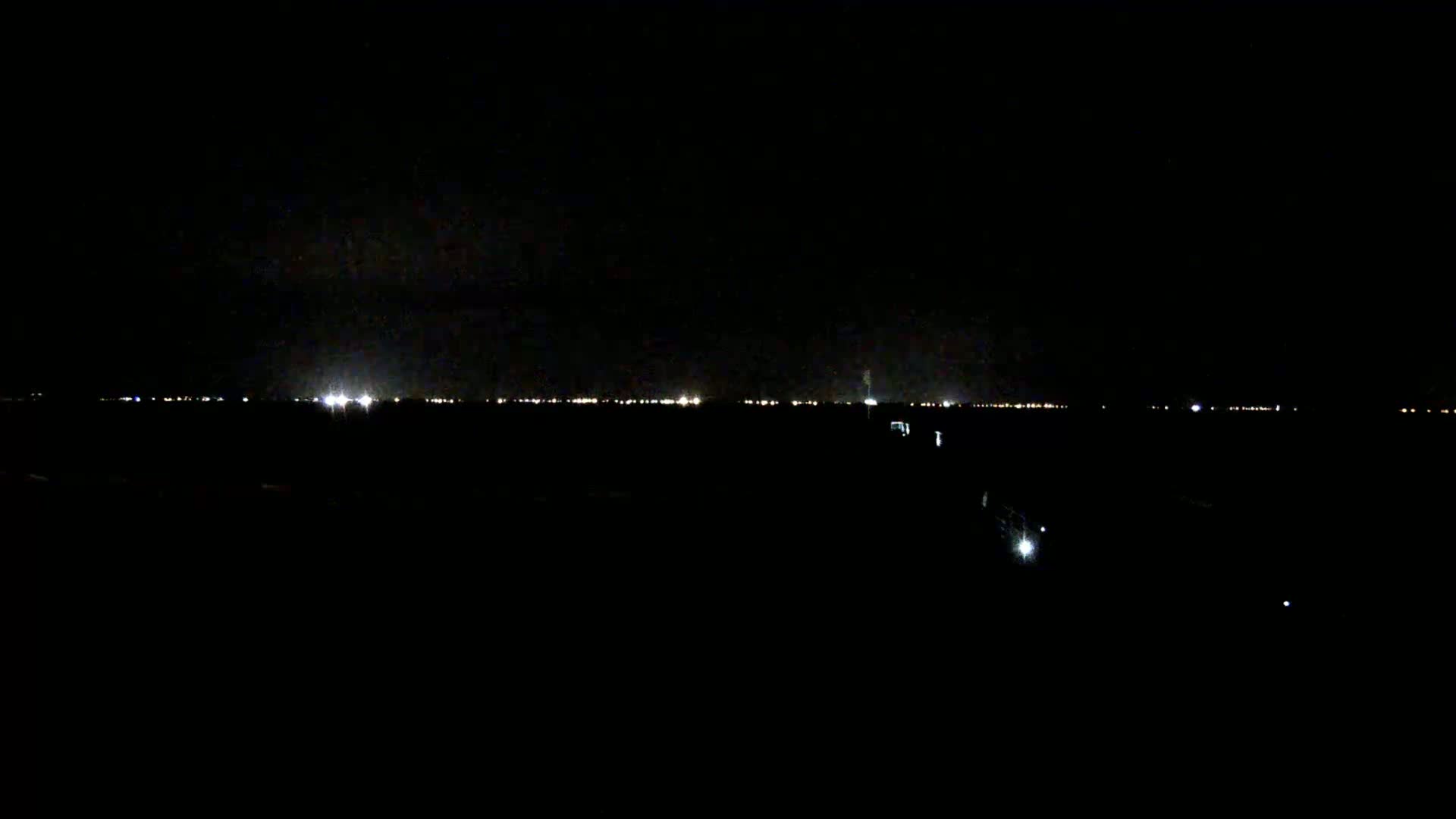 A dark, nighttime scene shows a distant line of city lights on the horizon.