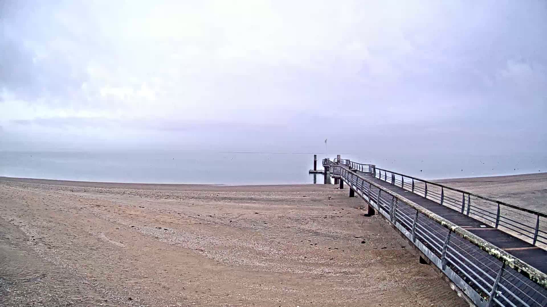 A long pier extends from a sandy beach into a calm, foggy sea.