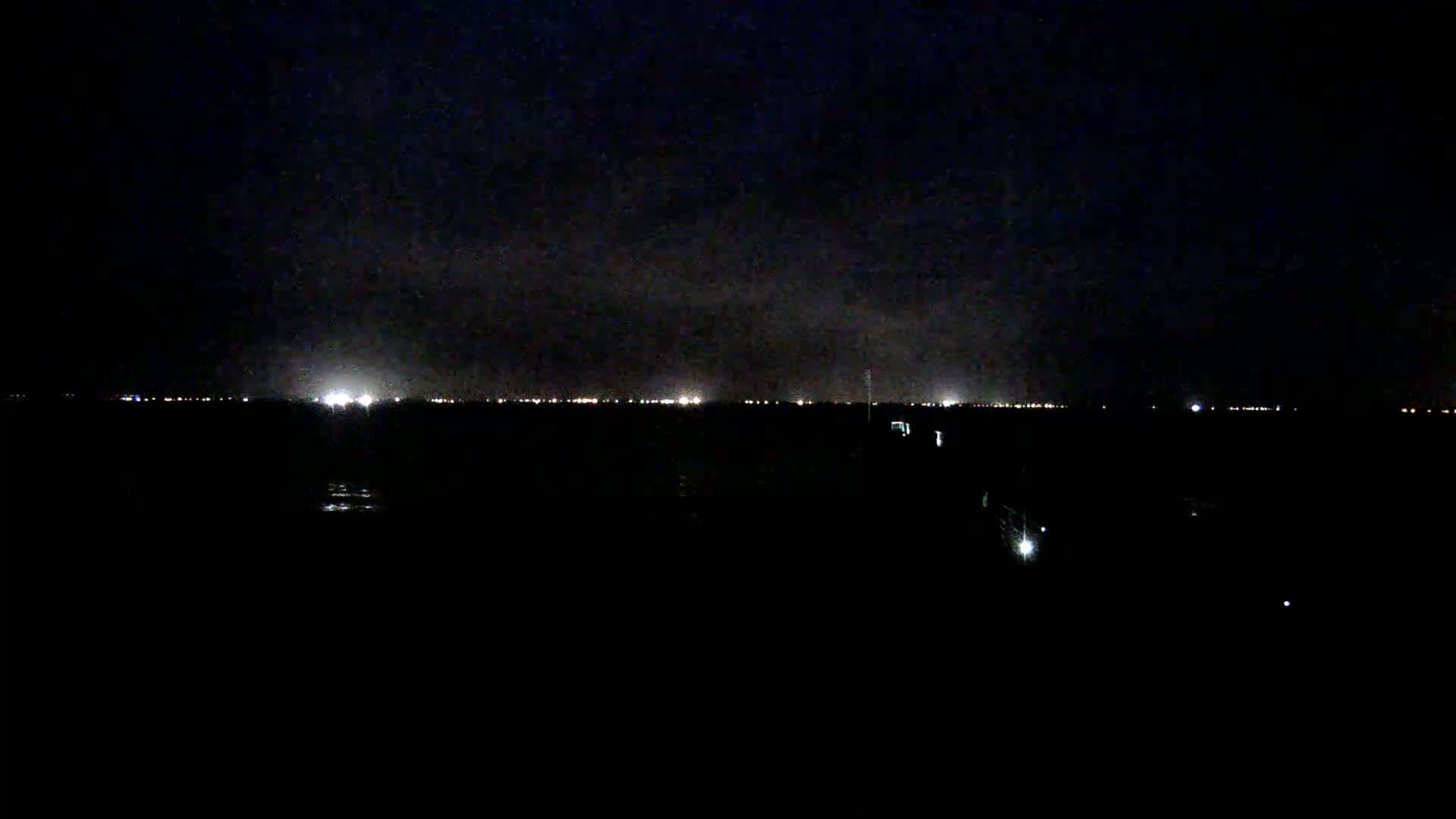 A dark, nighttime landscape shows a distant line of lights under a cloudy sky.
