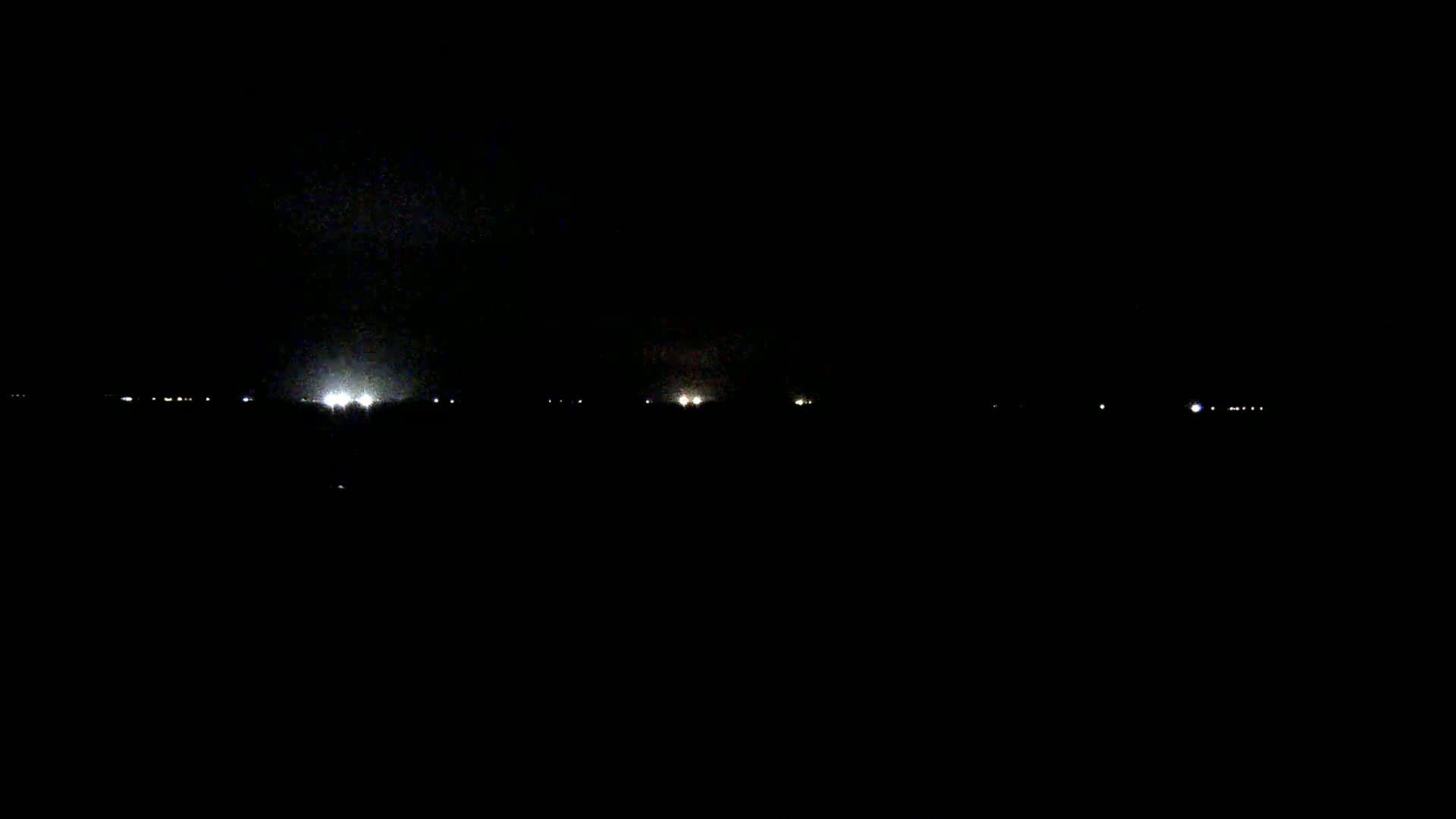 A dark, nighttime scene shows a distant line of faint lights on the horizon.