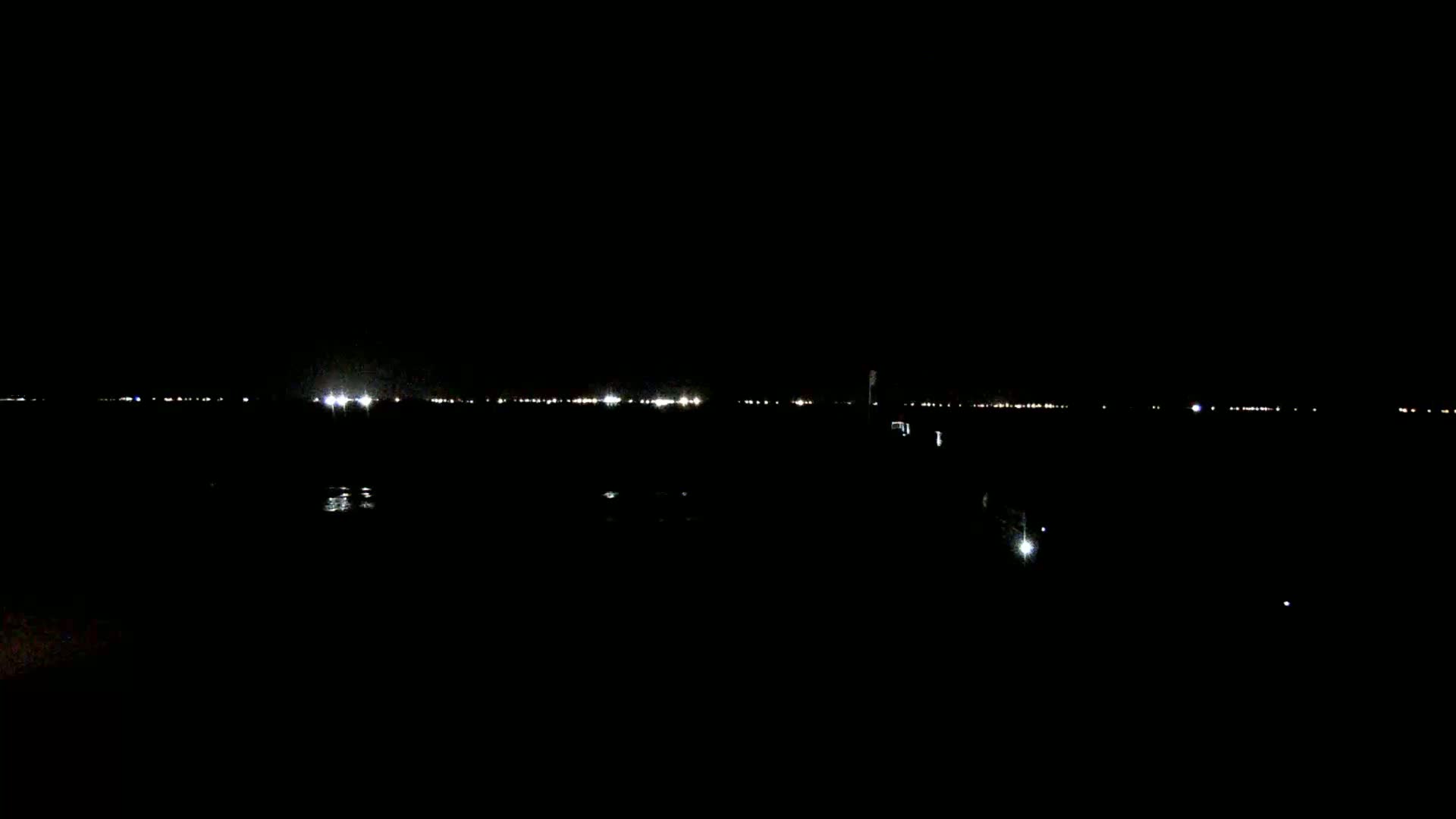 A dark, nighttime scene shows a distant line of lights across a body of water.