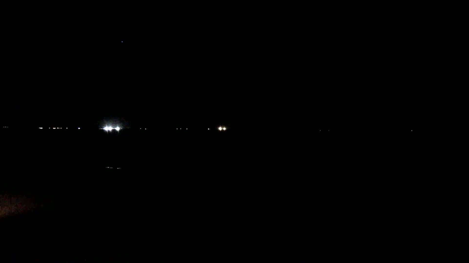 A dark, nighttime scene shows several faint lights in the distance, likely from vehicles or buildings.