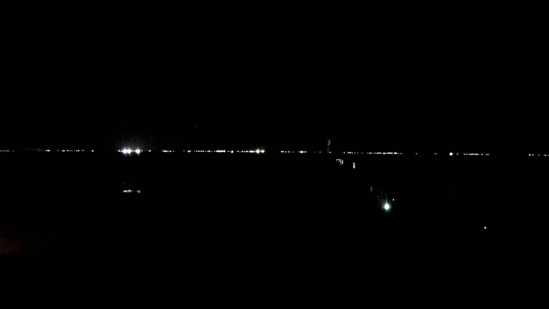 A dark, nighttime scene shows a distant line of lights across a body of water.