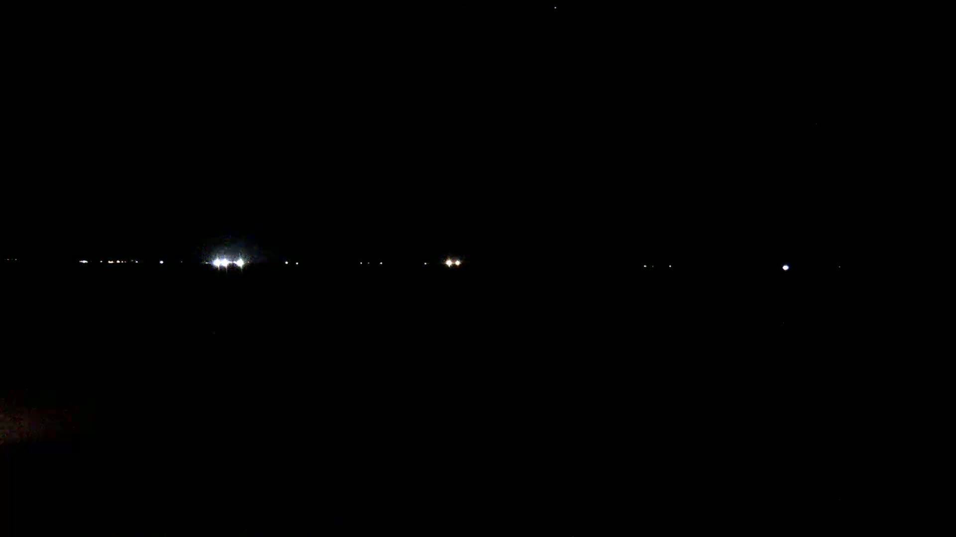 A dark, nighttime scene shows a distant line of faint lights on the horizon.