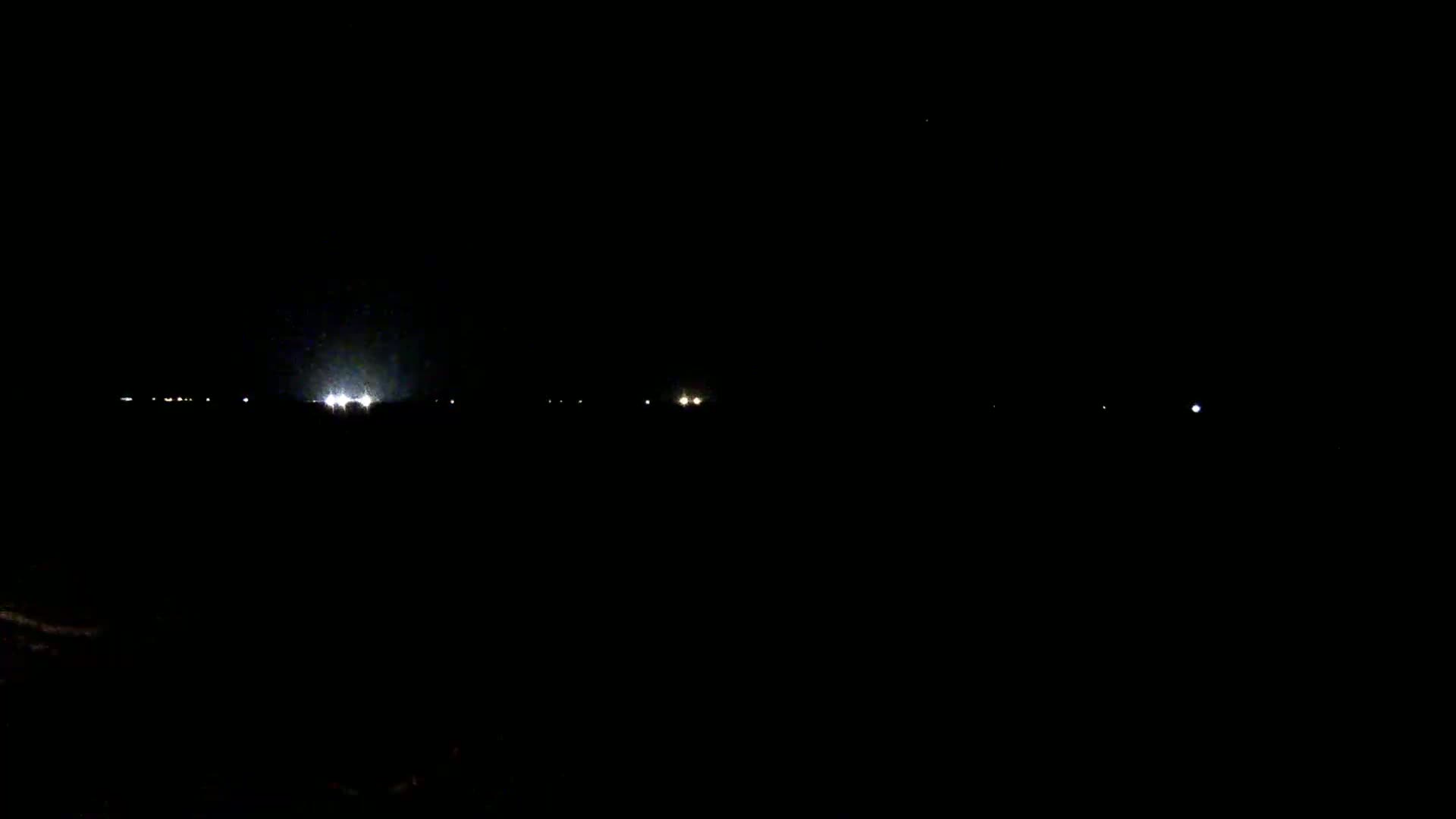 A dark, nighttime scene shows a few distant lights on the horizon under a clear, dark sky.