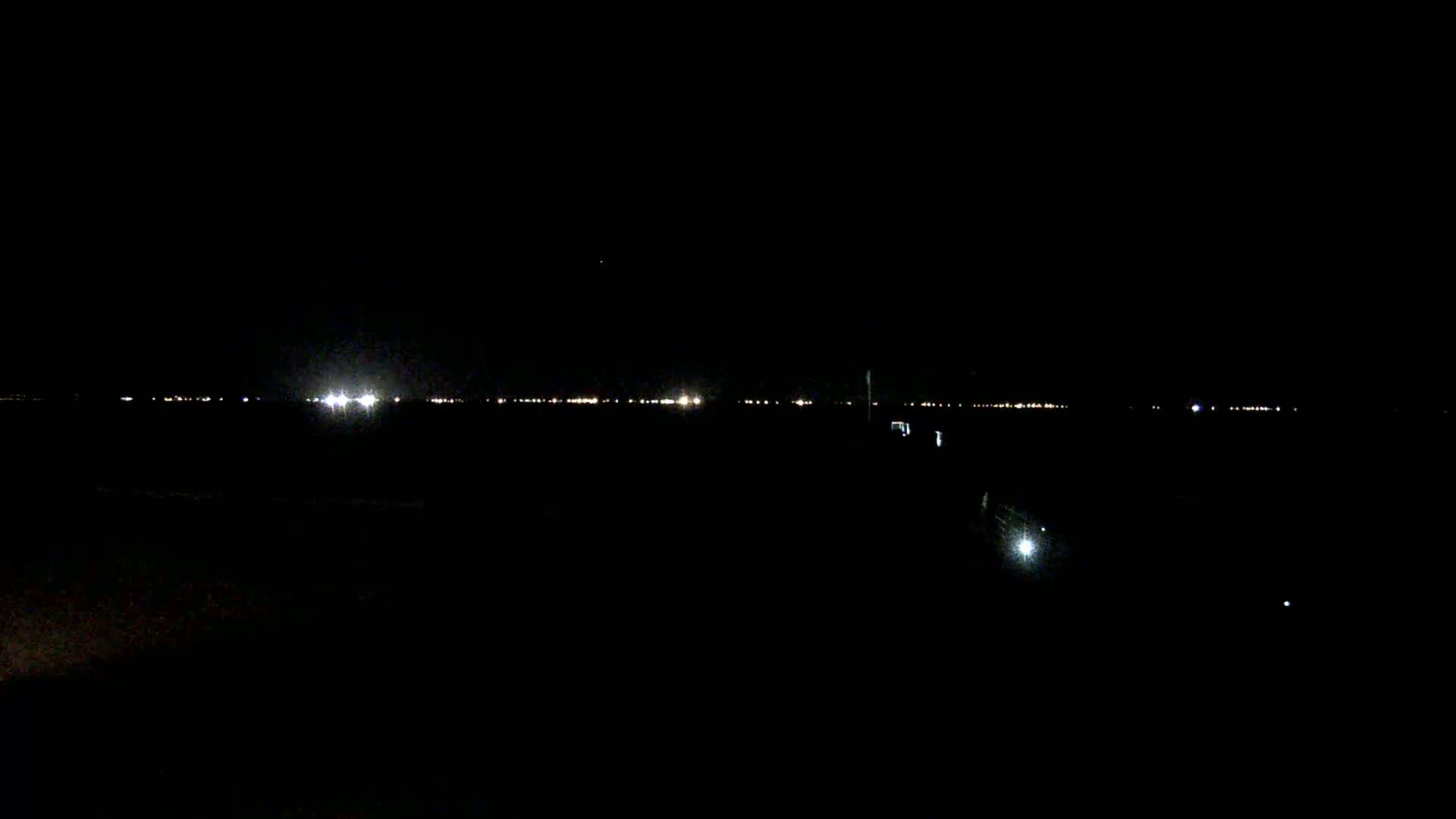 A dark, nighttime landscape shows a distant line of city lights on the horizon.