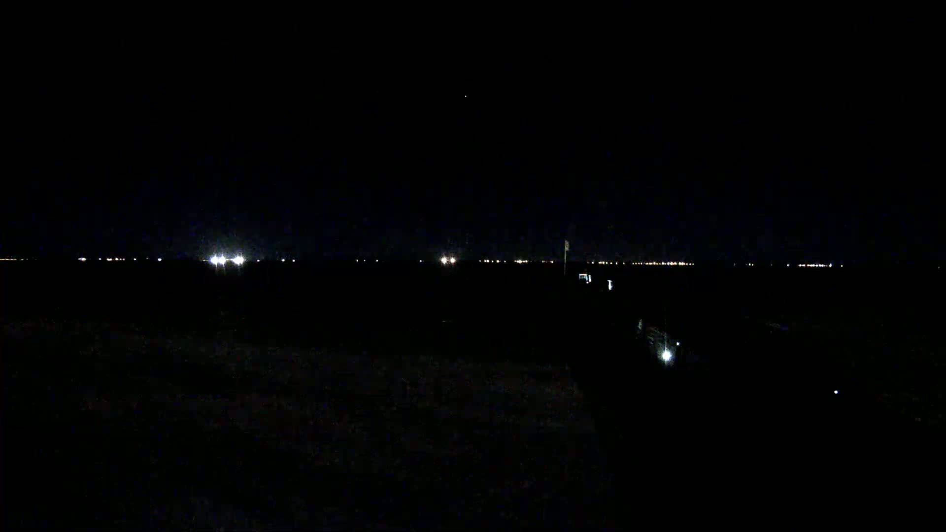A dark, nighttime scene shows a distant line of lights on the horizon.