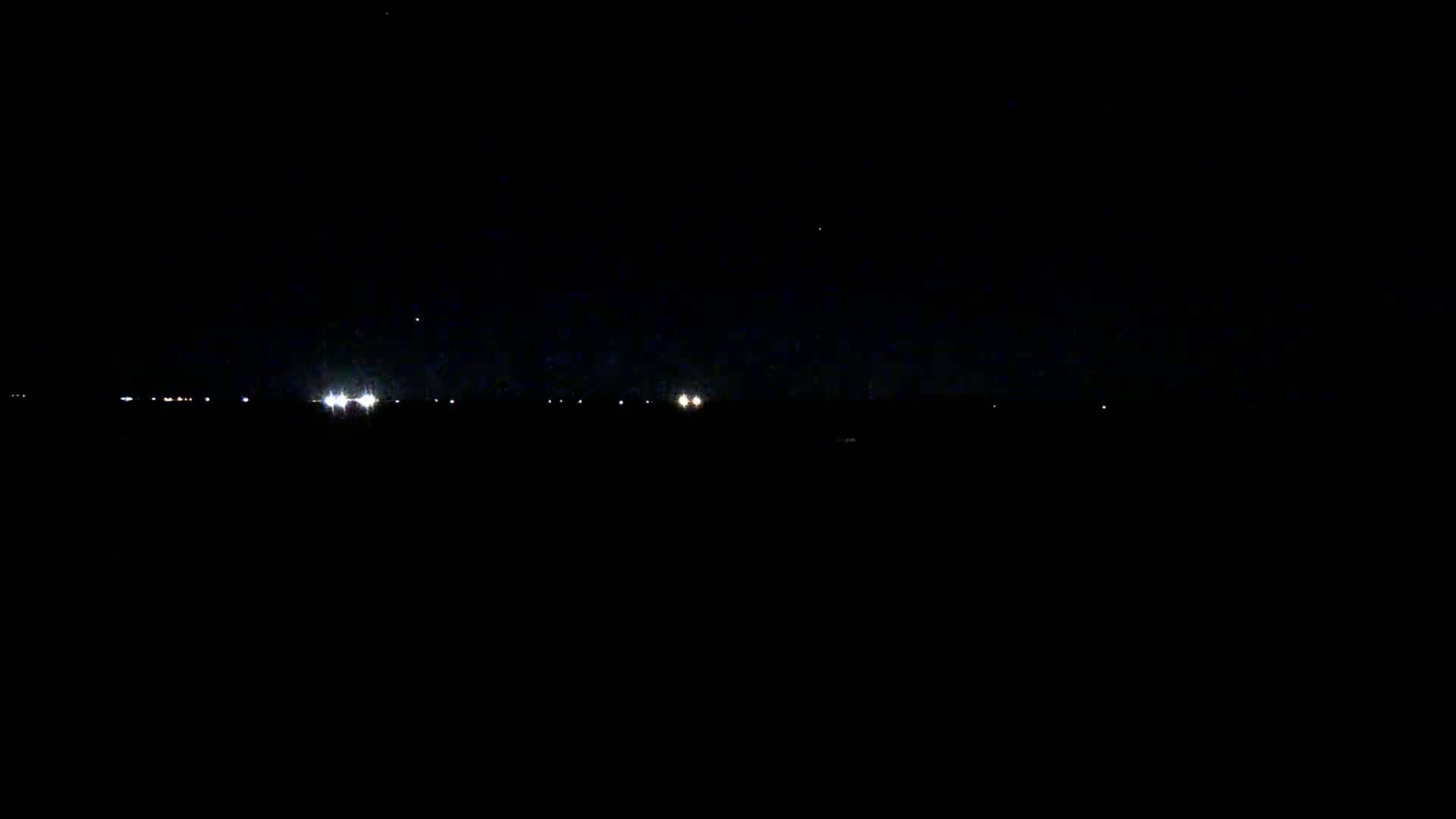 A dark, nighttime scene shows a few distant lights on the horizon under a clear, star-studded sky.