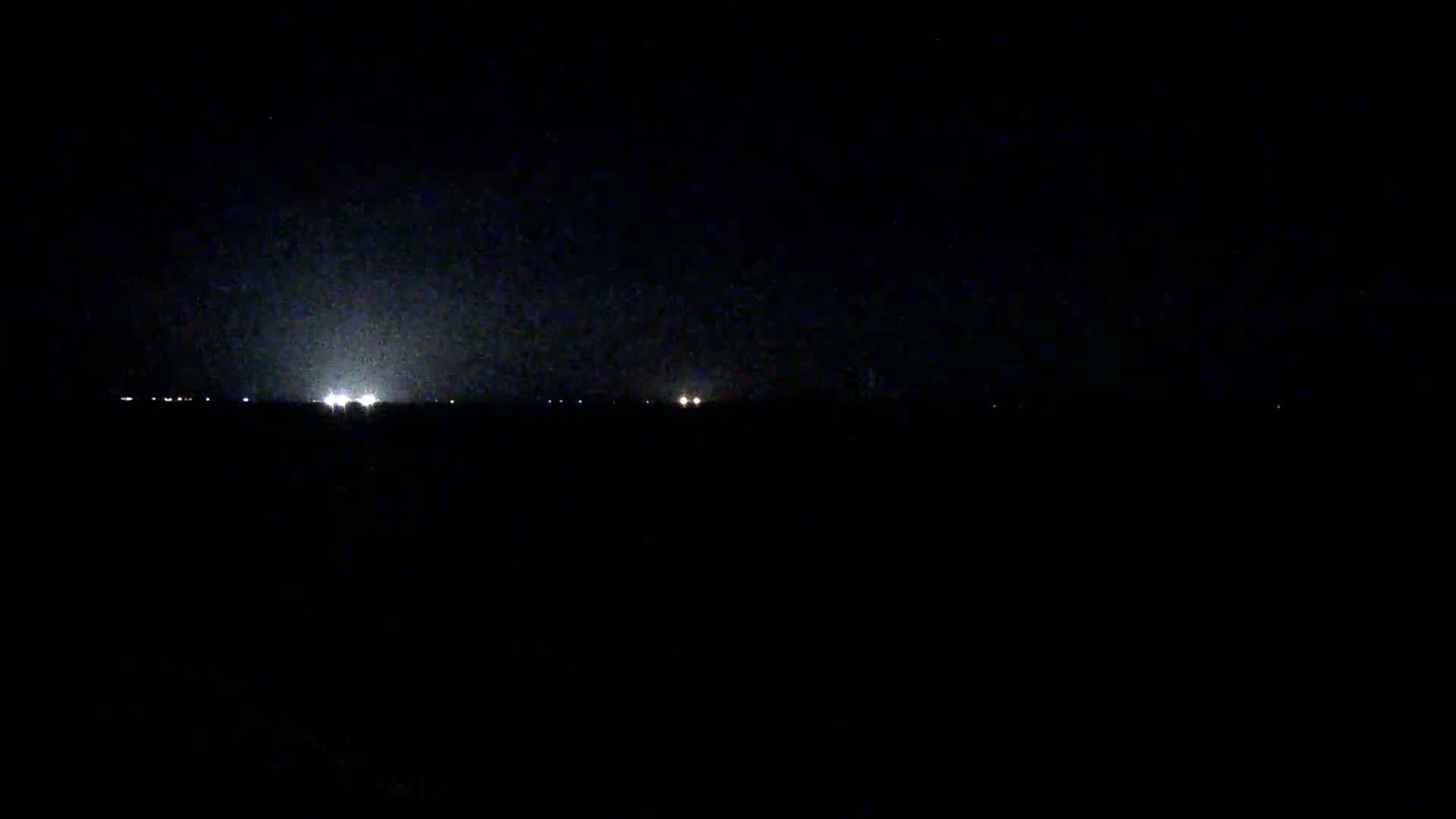 A dark, nighttime landscape is visible, showing a faint, hazy glow on the horizon and a few scattered lights in the distance.