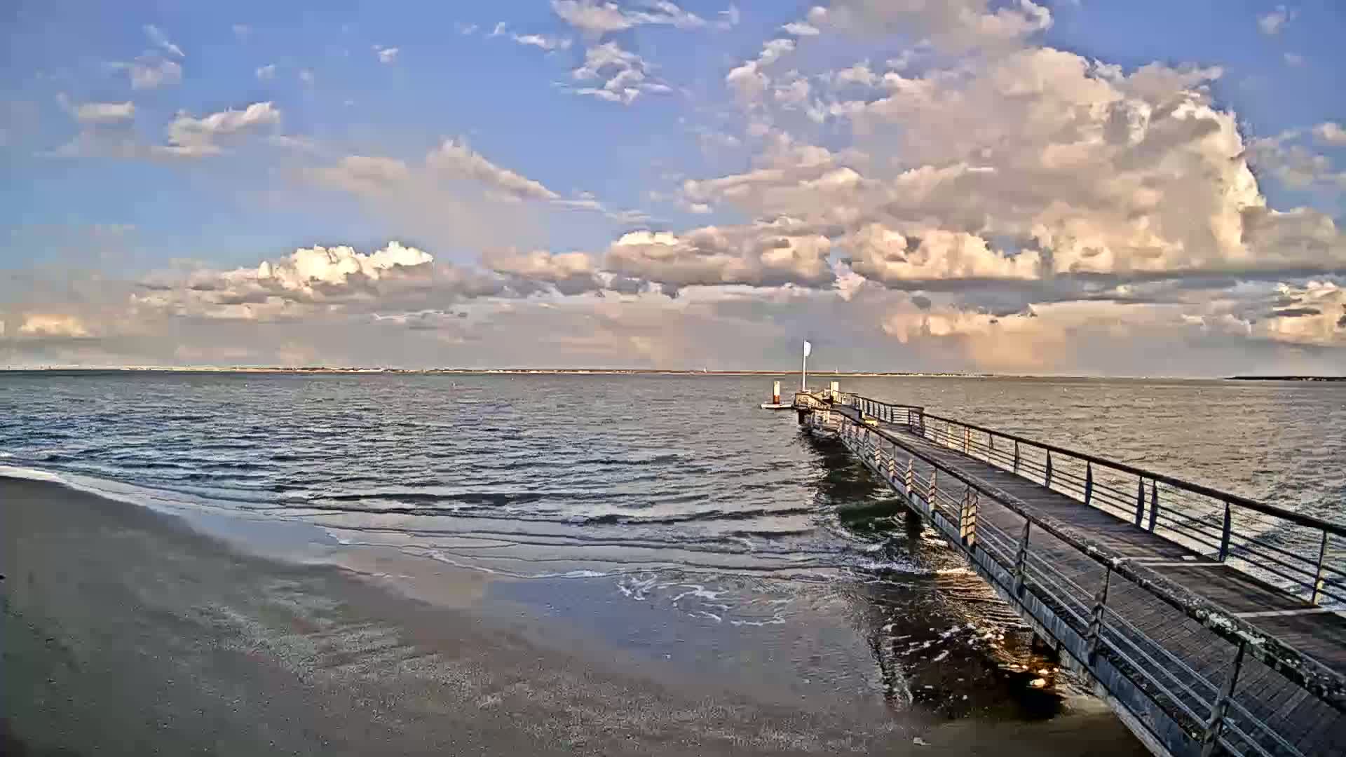 A long pier extends into a calm body of water under a partly cloudy sky.
