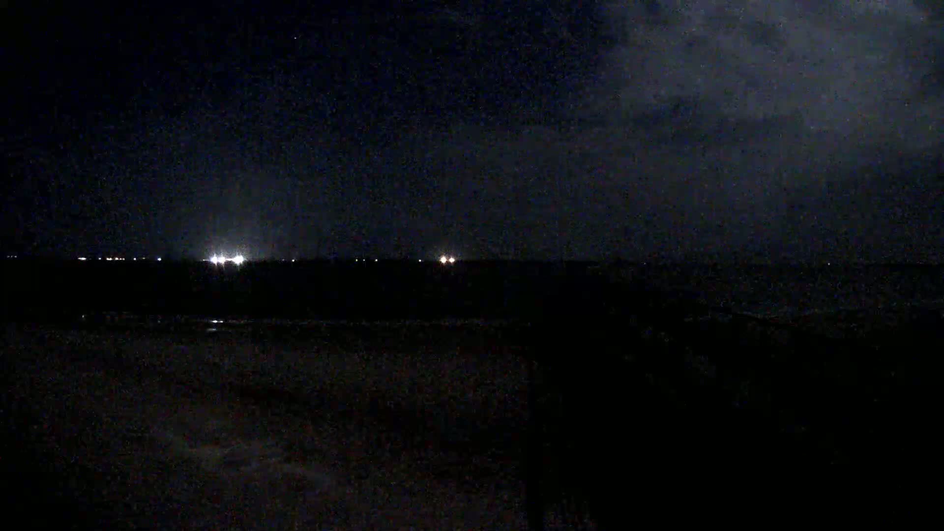 A dark, nighttime scene shows a distant line of lights under a cloudy sky.