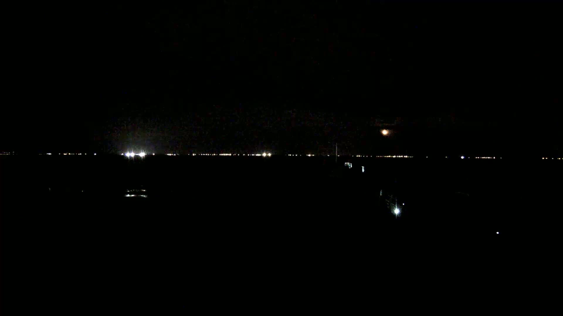 A nighttime view of a distant cityscape illuminated by lights, with a moon visible in the sky.