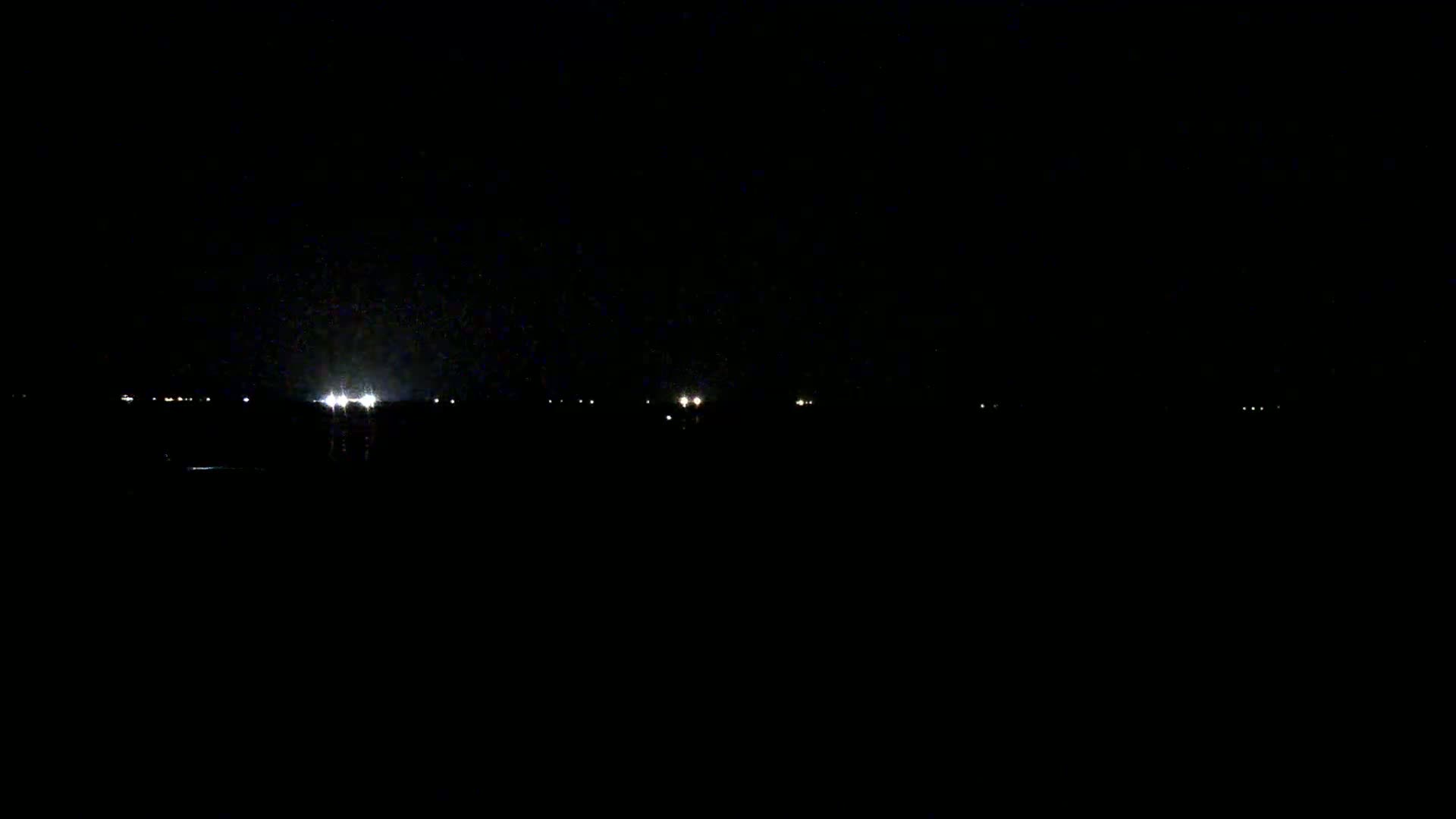 A dark, nighttime scene shows a few faint lights in the distance under a possibly slightly hazy sky.