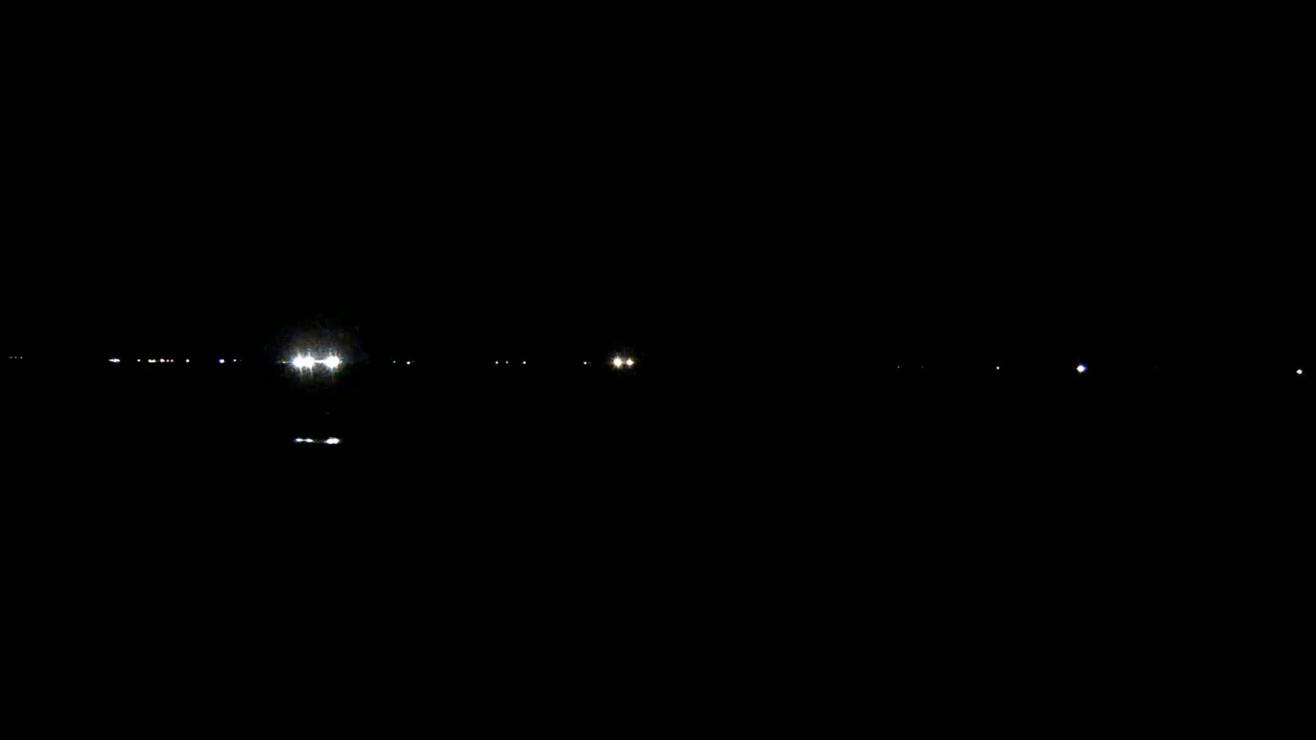 A dark nighttime scene shows a line of faint lights in the distance, possibly from vehicles or buildings.