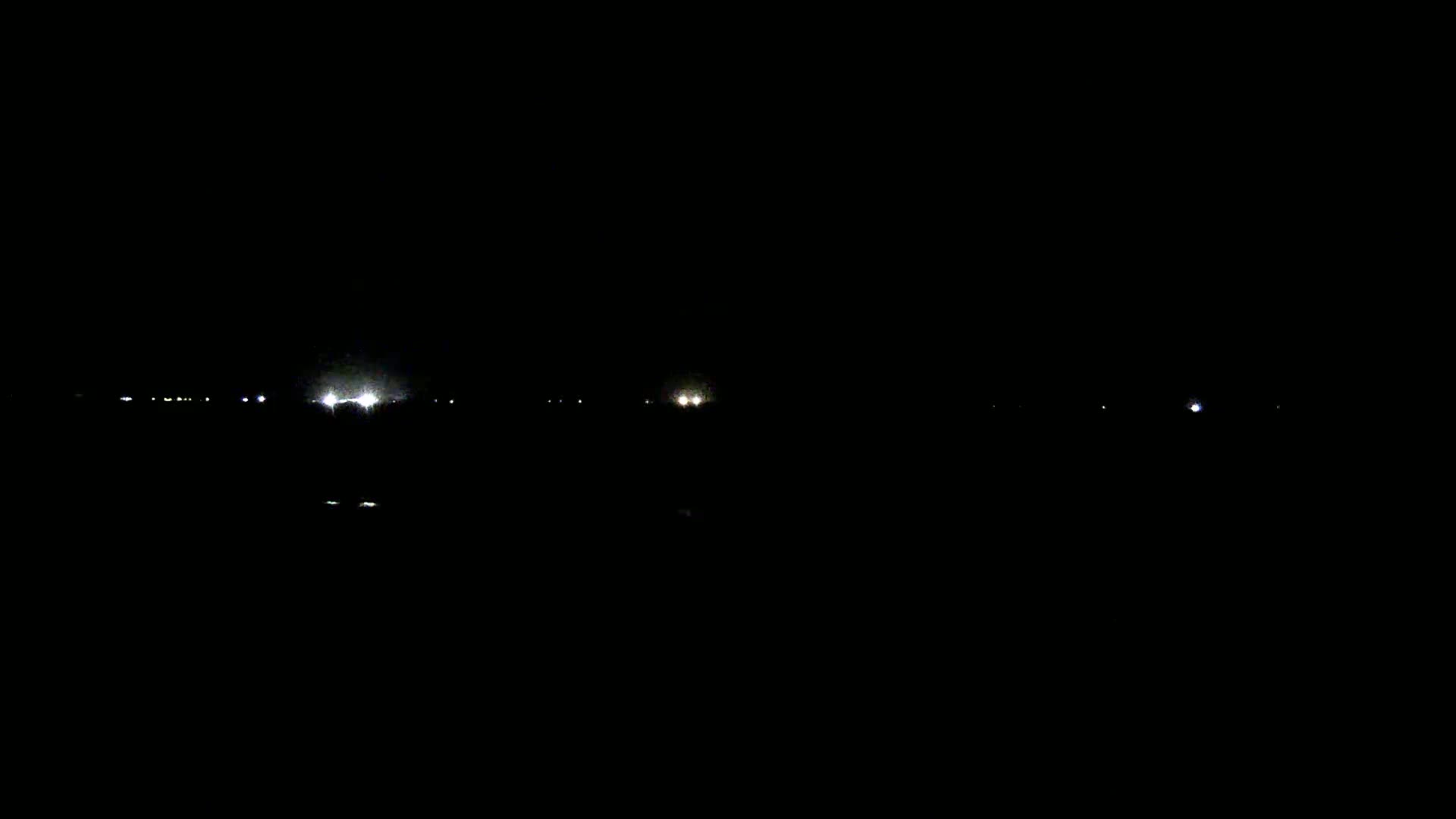 A dark nighttime scene shows a few distant lights on a horizon line.