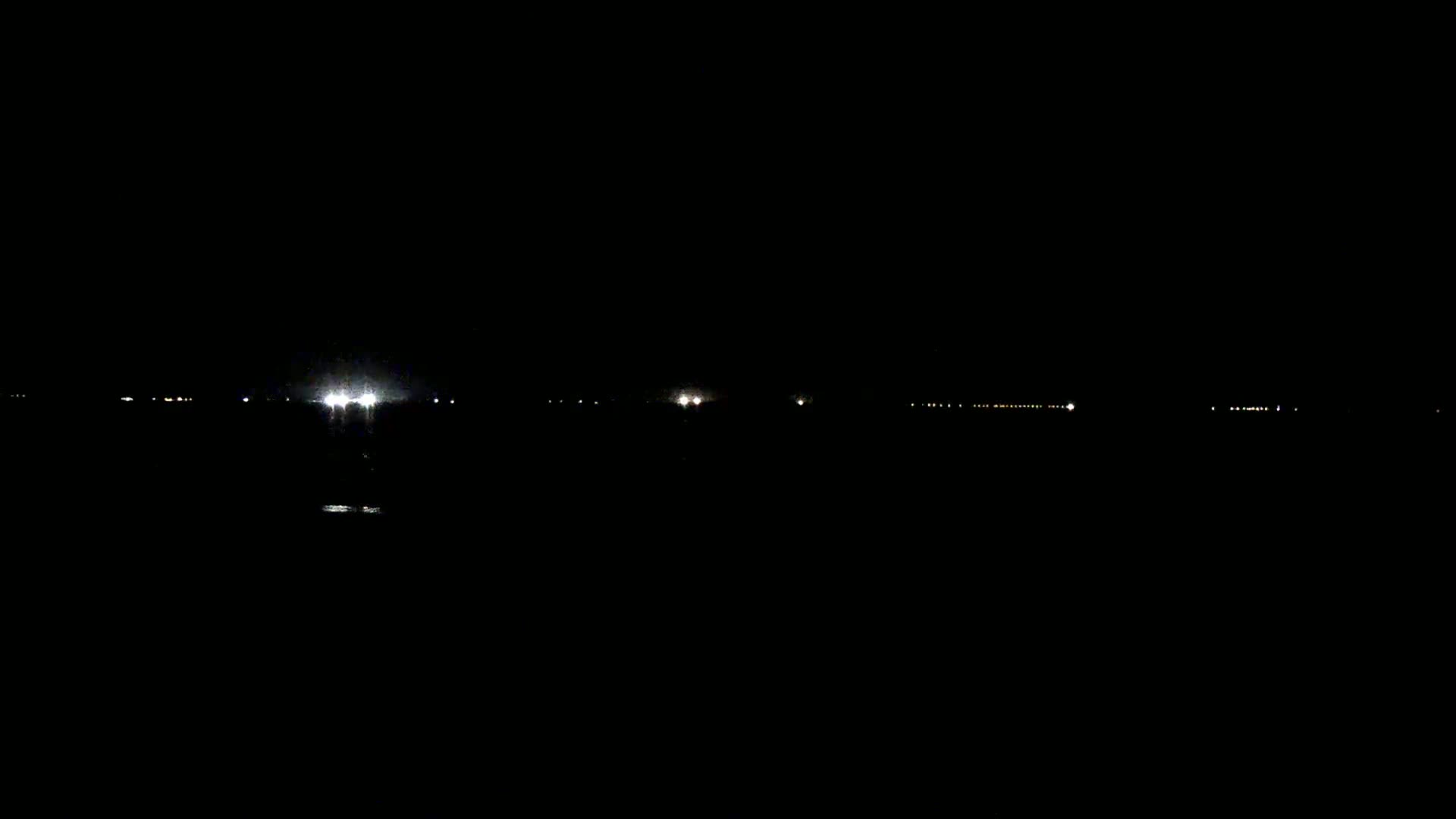 A dark, nighttime scene shows a faint line of distant lights reflecting on dark water.