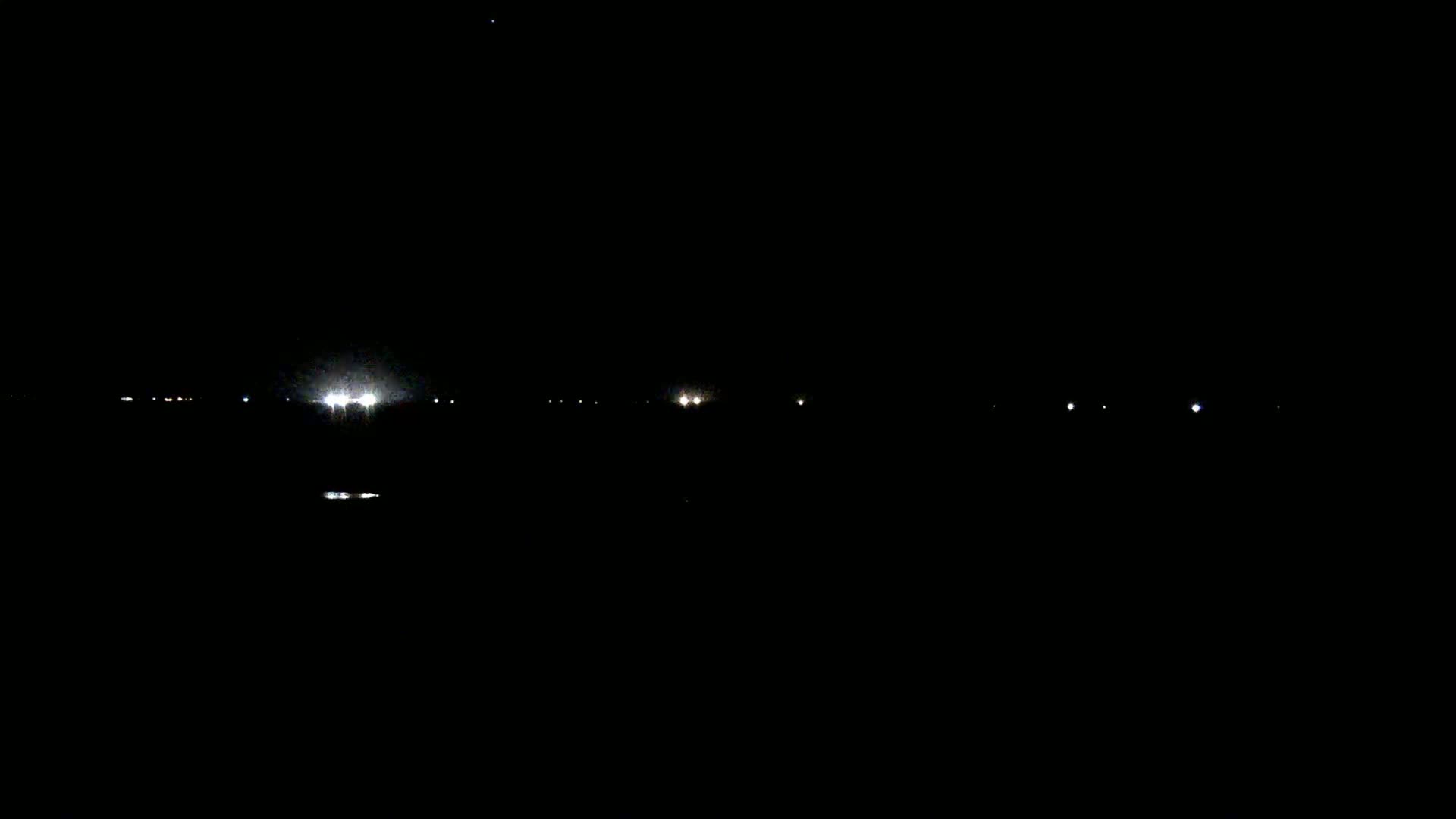 A dark, nighttime scene shows a distant line of faint lights on the horizon.