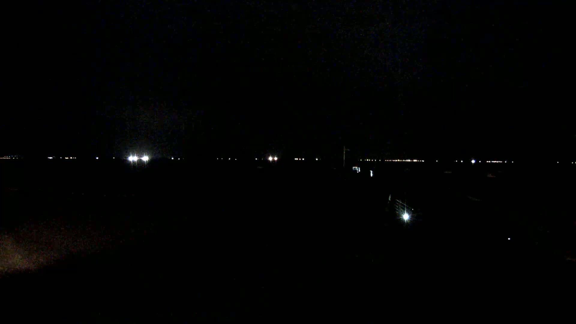 A dark, nighttime landscape shows a line of distant lights.