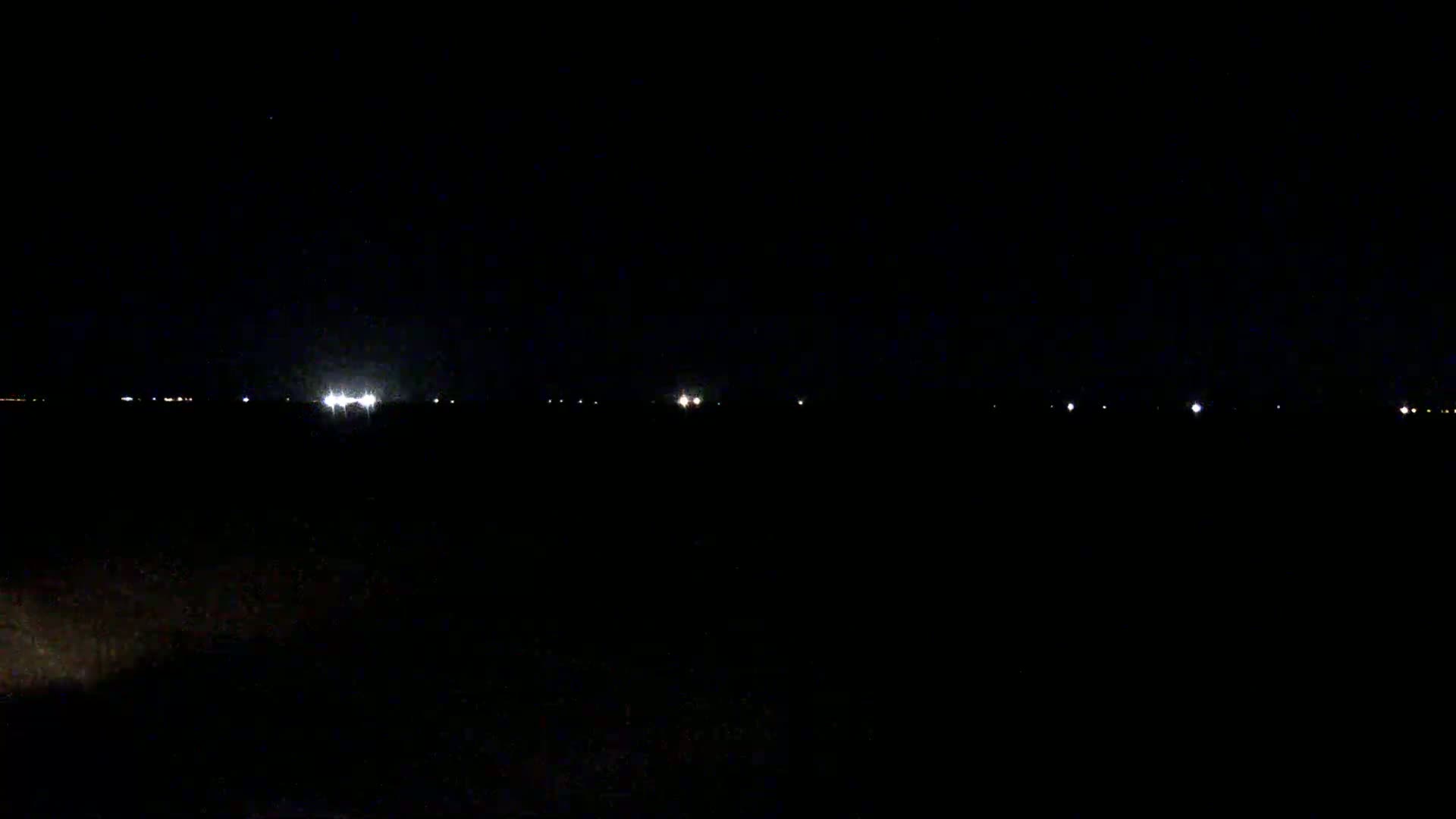 A dark, nighttime landscape is visible, showing a line of distant lights on the horizon under a clear, dark sky.